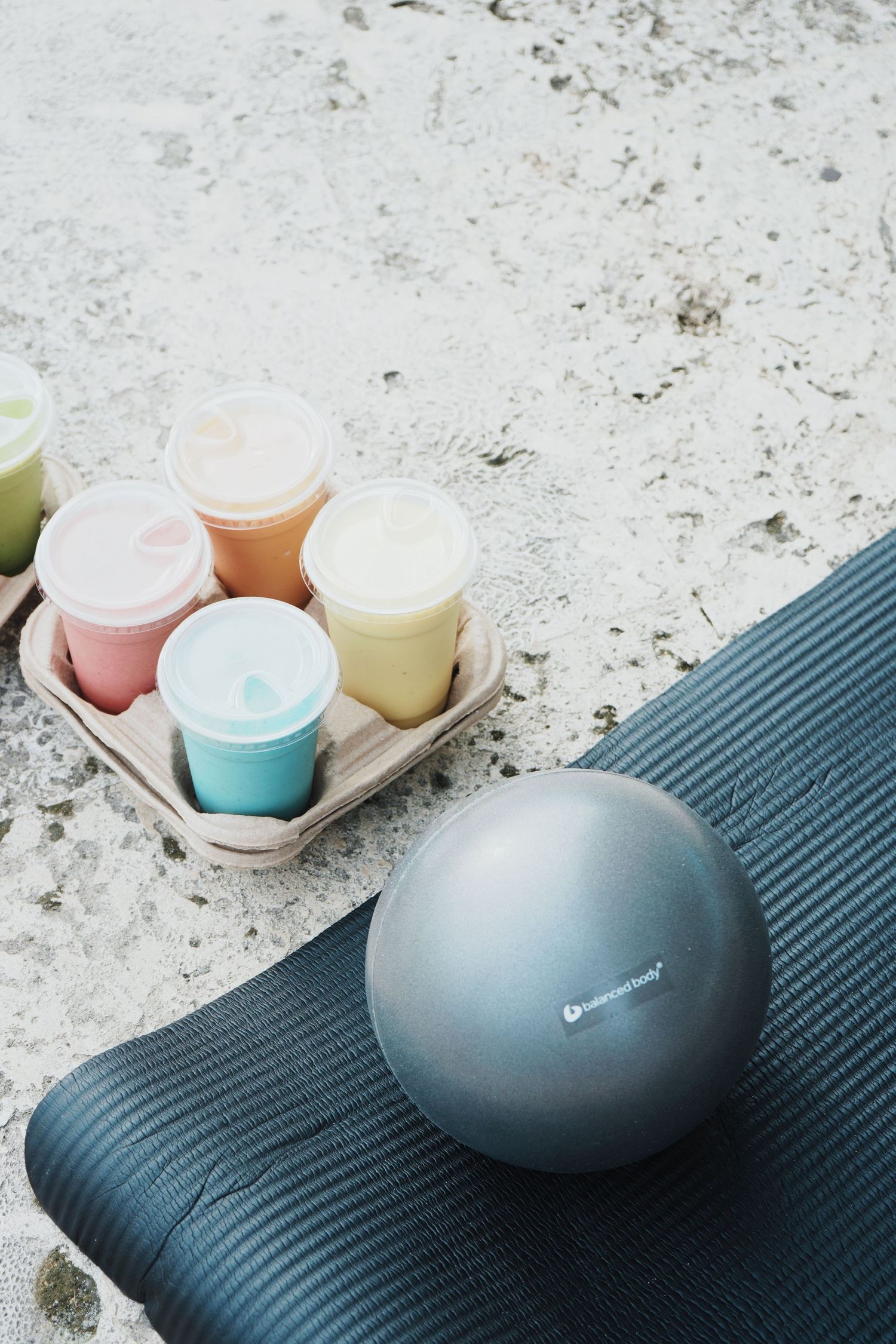 Colorful smoothies and a dark gray stone diffuser arranged on a textured navy blue yoga mat against a white surface.