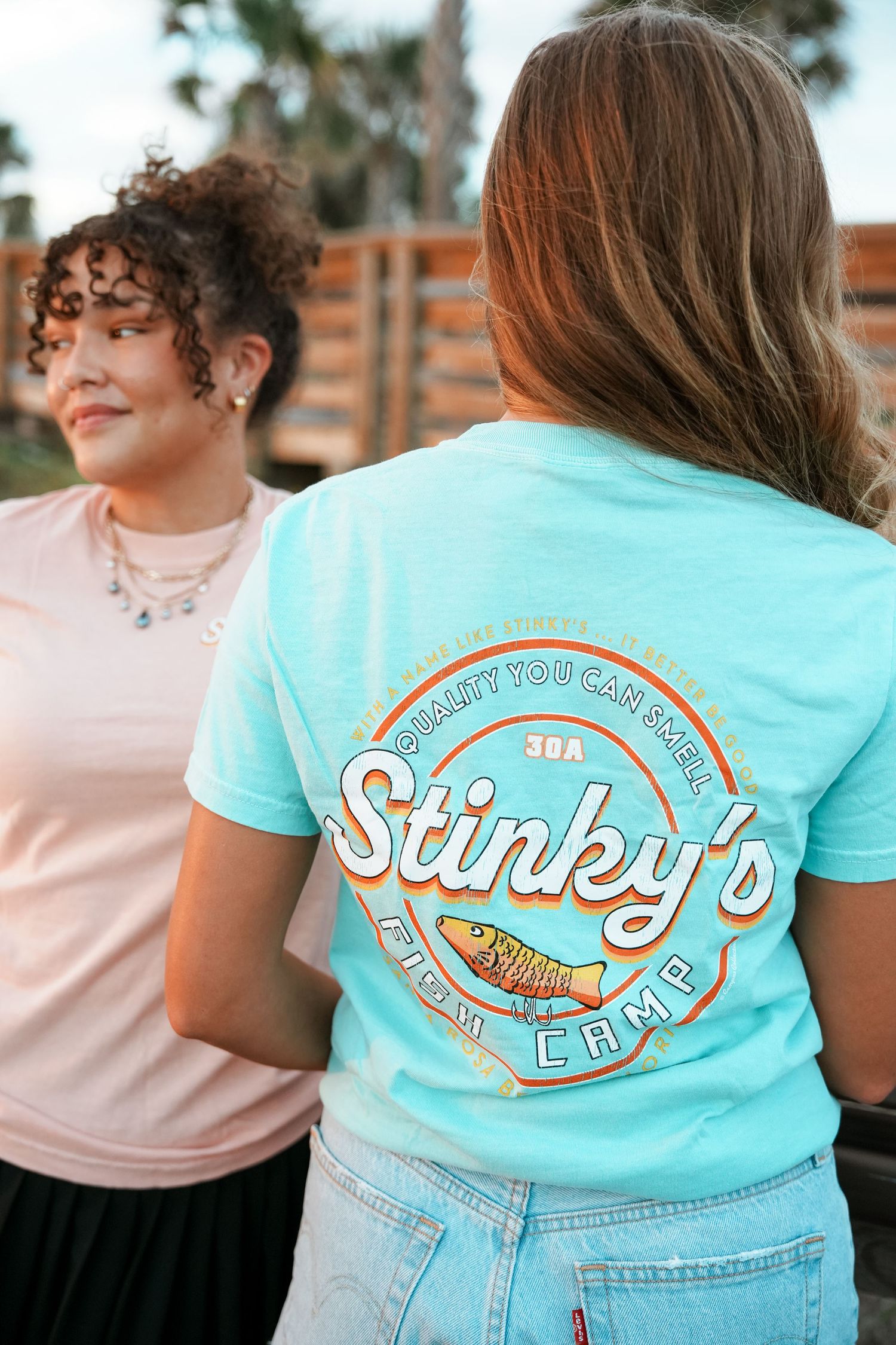 People wearing turquoise and pink t-shirts with vintage-style Sankey's Grill logo design on the back.