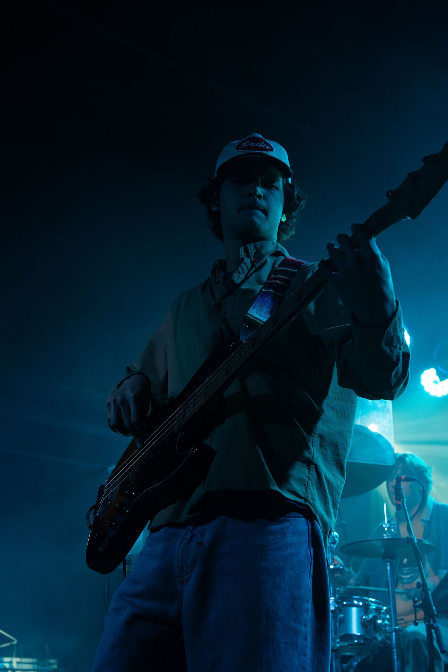 Musicians perform on stage in moody blue lighting with silhouetted figures holding instruments.