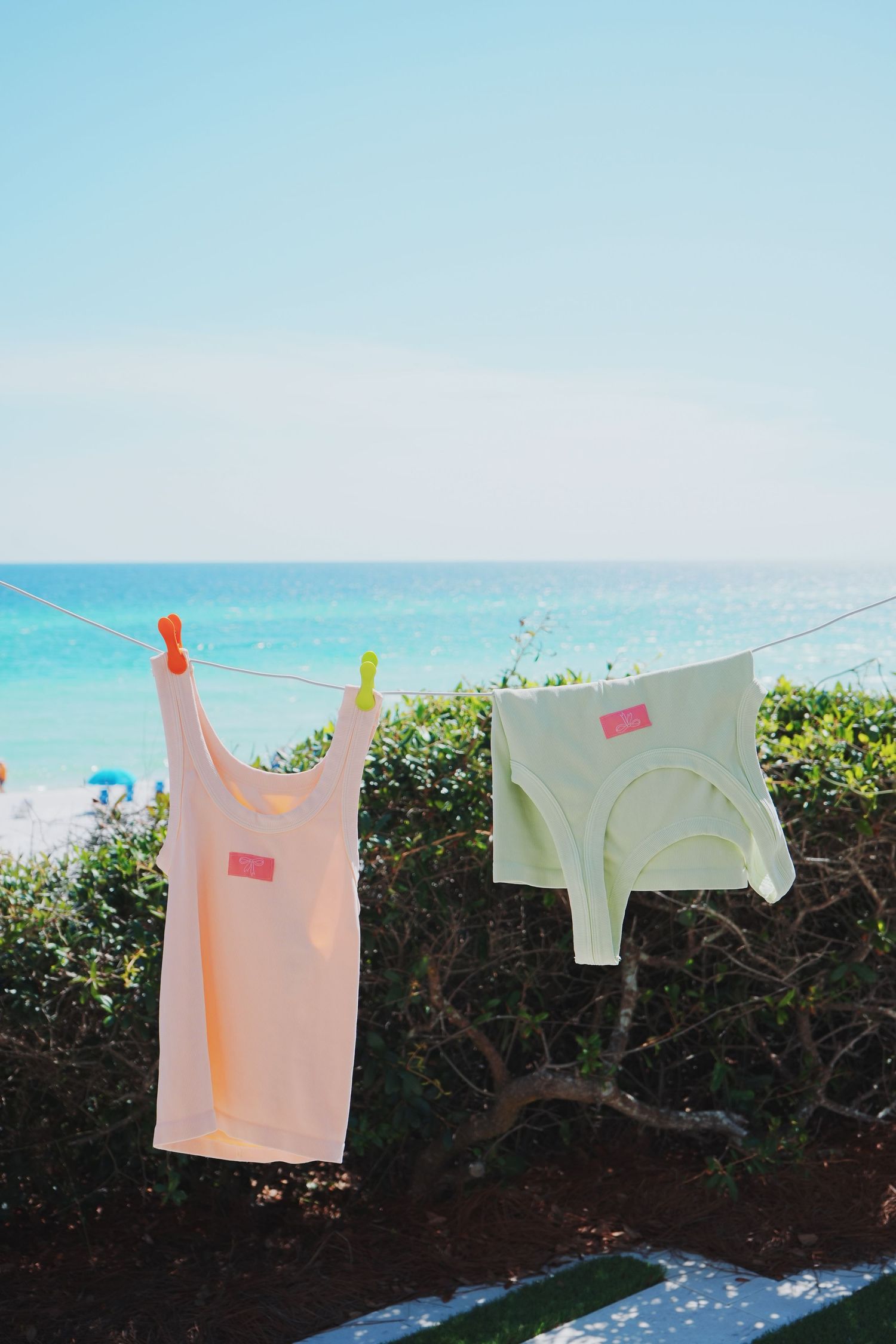 Pink and white tank tops hanging on a clothesline against an ocean backdrop on a sunny day.