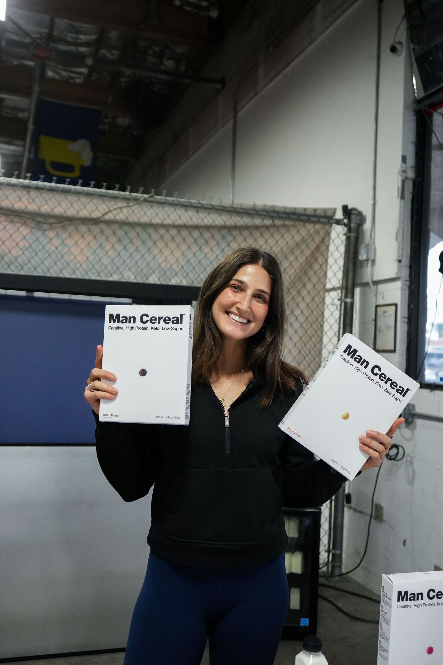 Person holding up Man Cereal branded packaging in an industrial setting.