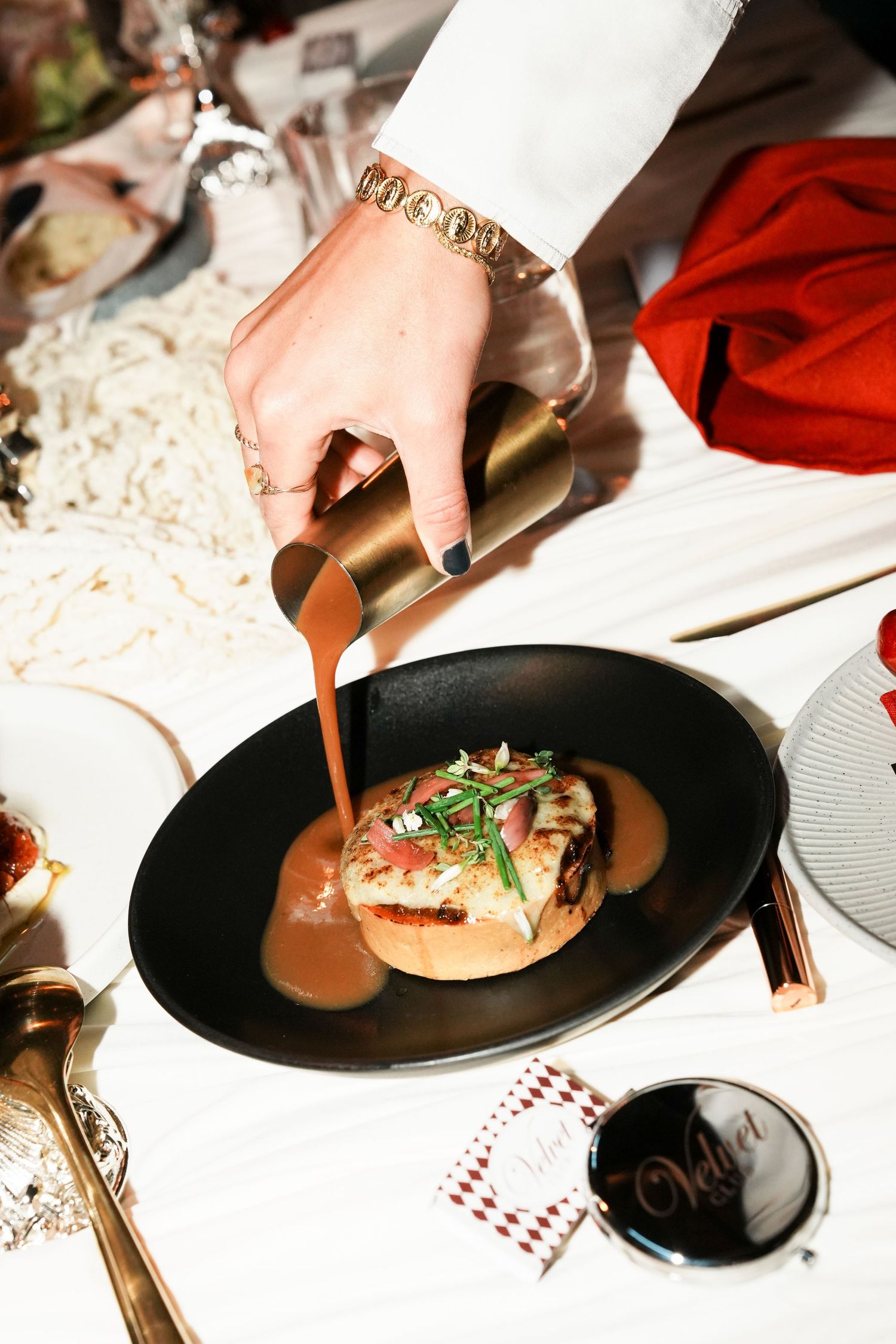 Elegant plating service with a hand pouring sauce over a gourmet dish in a black bowl at a fine dining event.