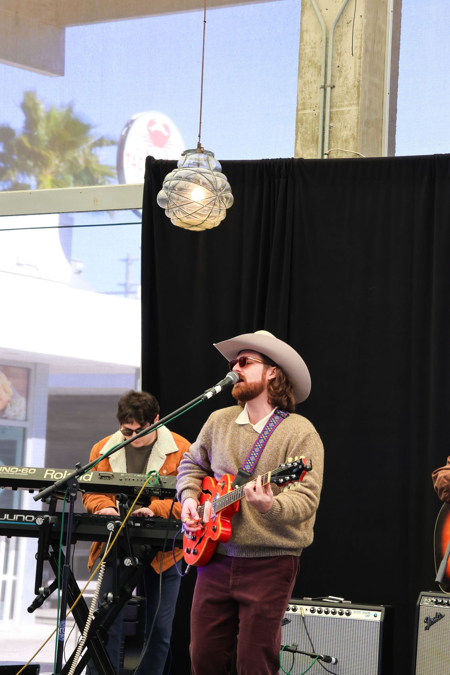 Country musician performing on stage with guitar wearing cowboy hat and sweater.
