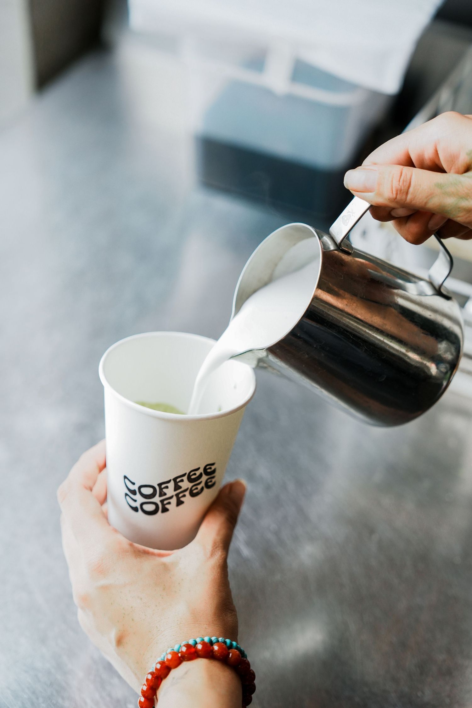 Barista pouring steamed milk into white paper coffee cups with a black coffee shop logo.