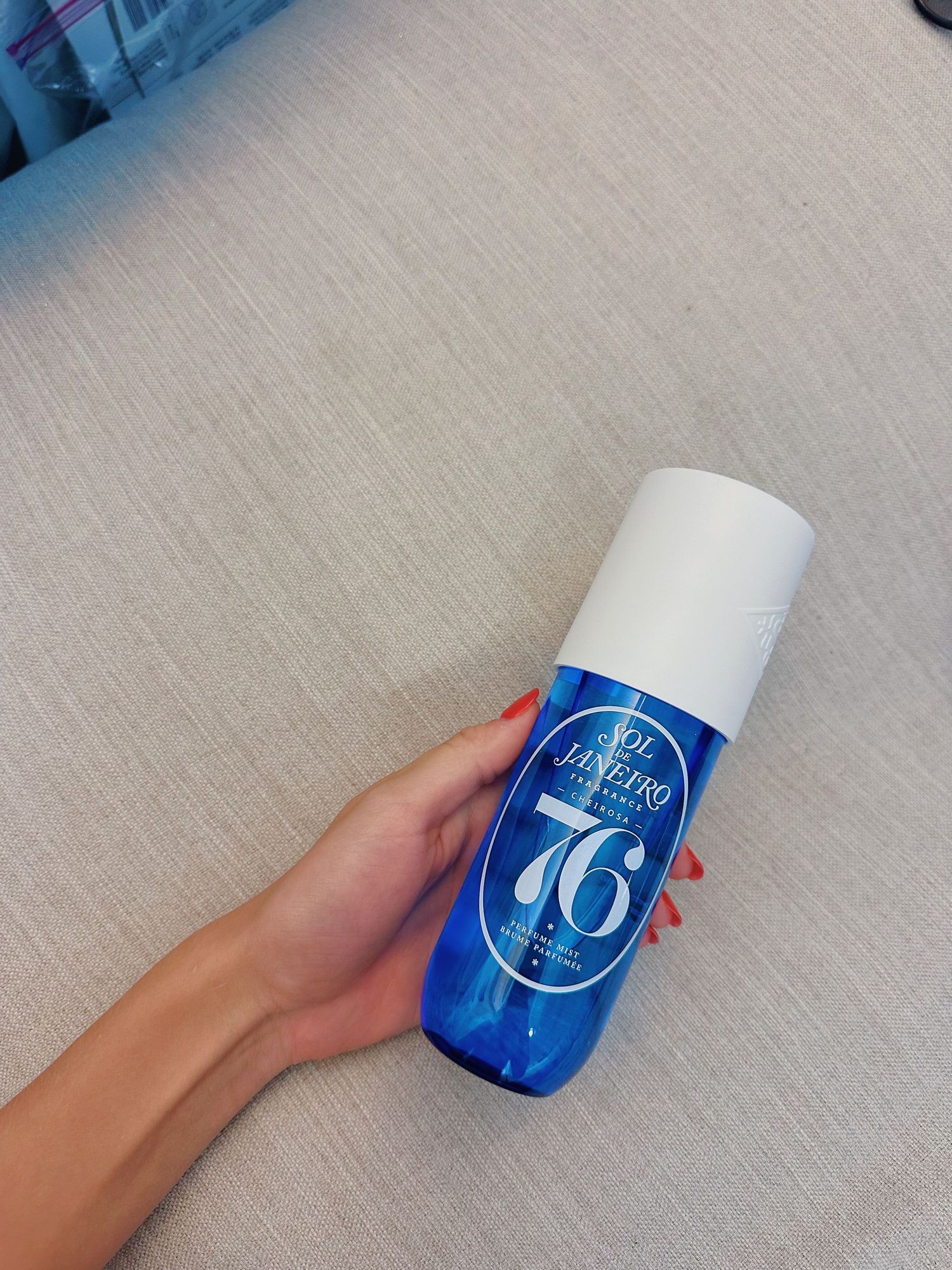 Hand holding blue and white bottle of 76 branded beauty product against grey background.