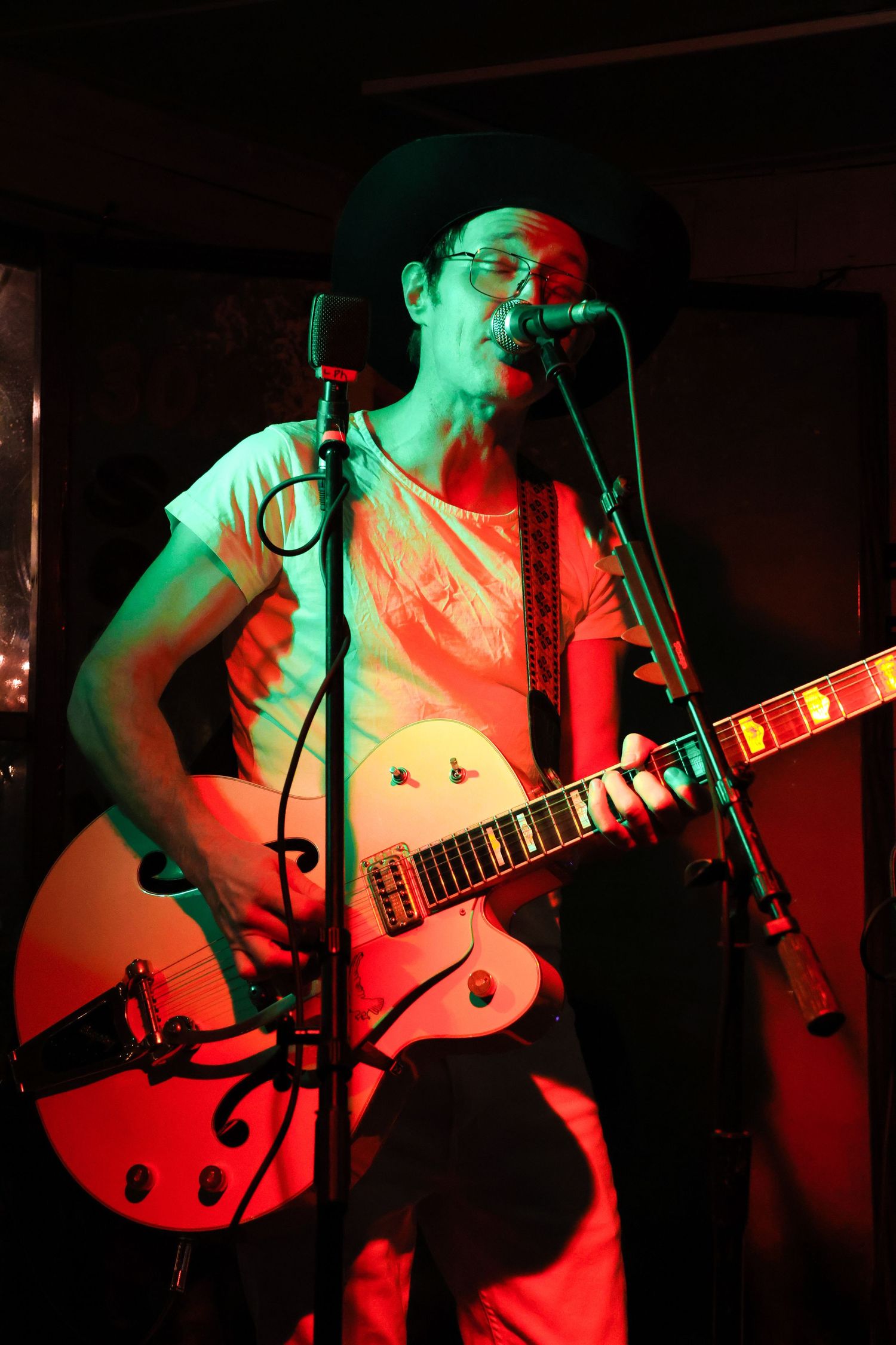 Musician playing electric guitar bathed in red and green stage lighting.