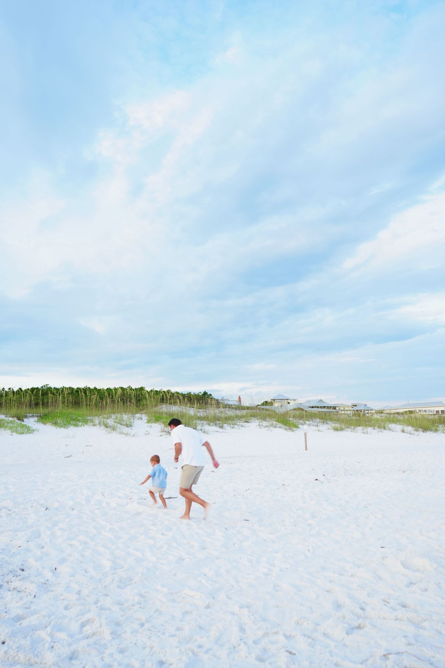 Footprints trail across pristine white sand beach under bright blue summer sky.