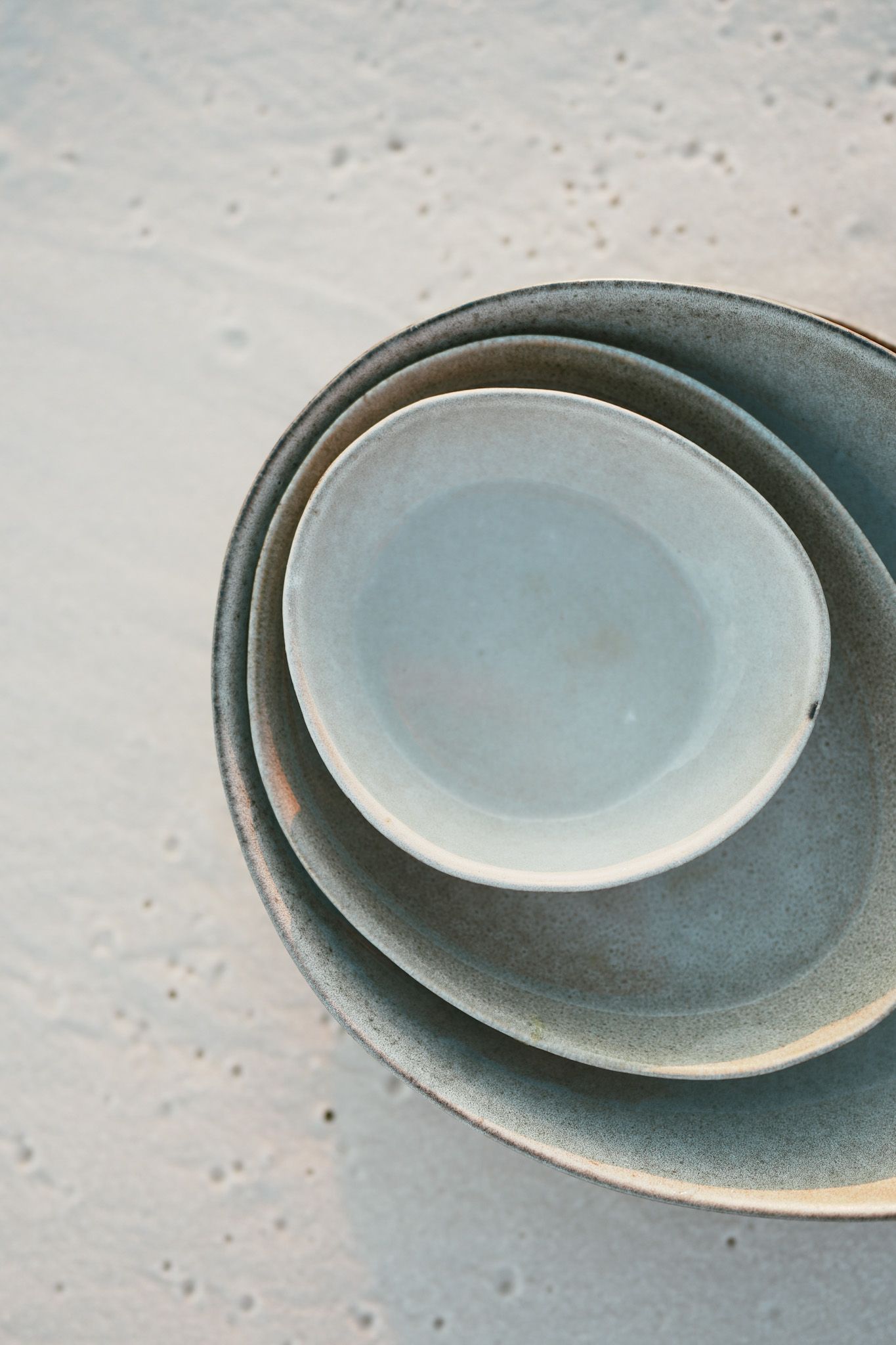 A collection of minimalist ceramic plates in muted blue and gray tones arranged in an overlapping pattern.