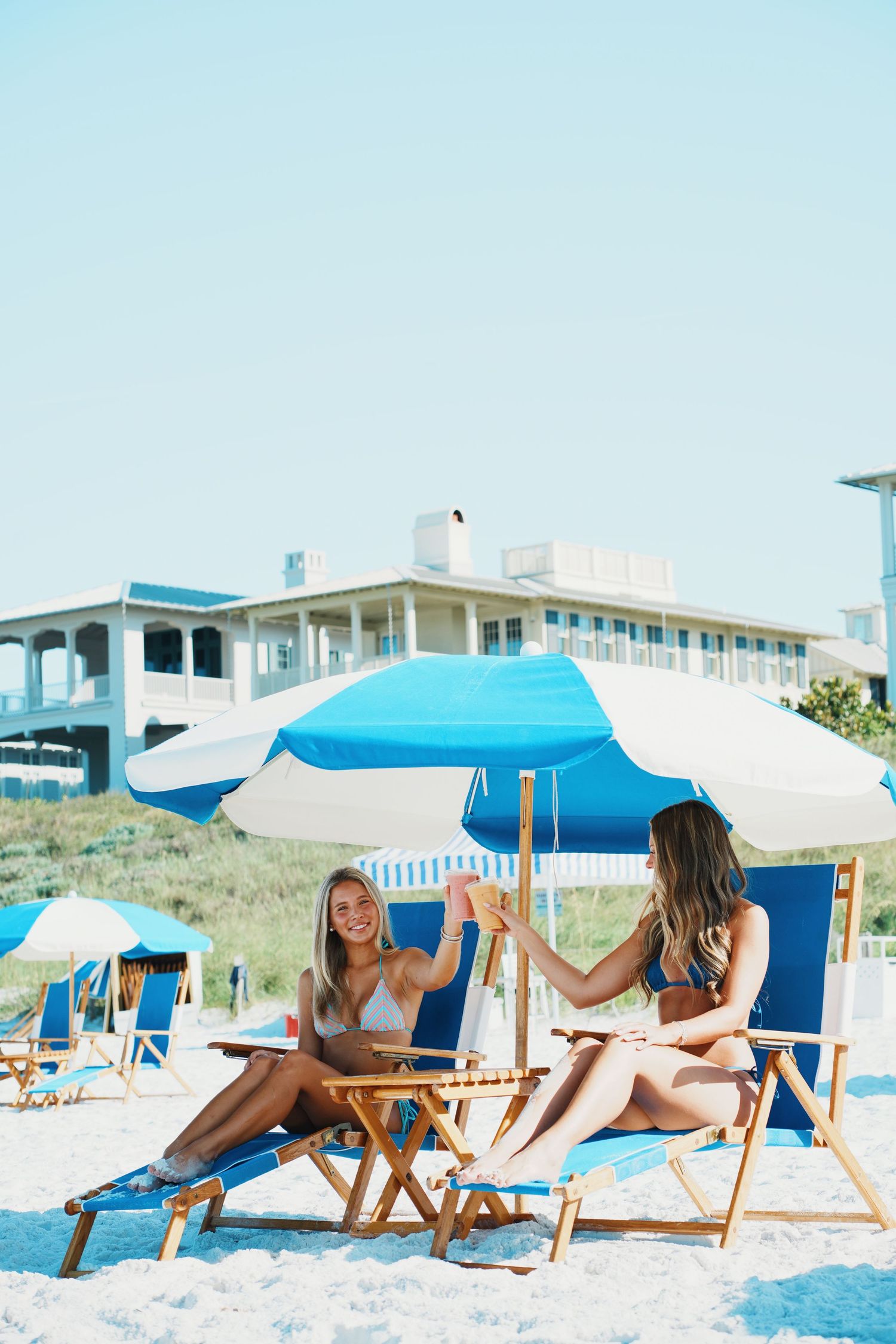 Friends relaxing under bright blue beach umbrellas on a sunny summer day at the beach.