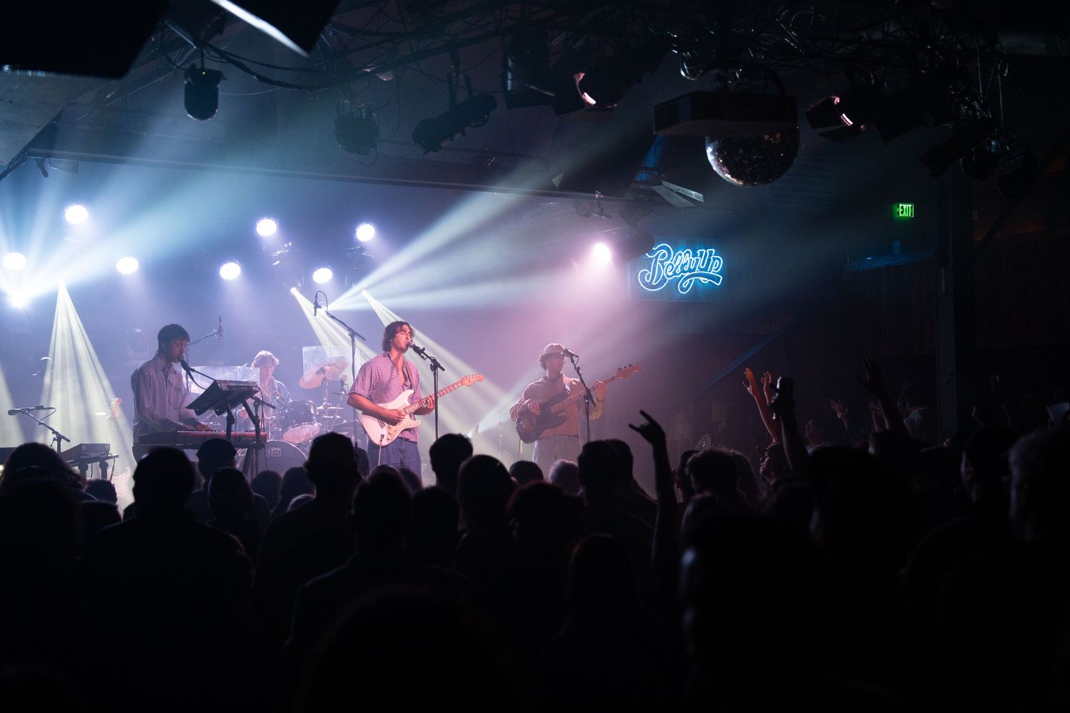 Silhouettes of musicians performing on stage with dramatic purple and blue concert lighting effects in background.