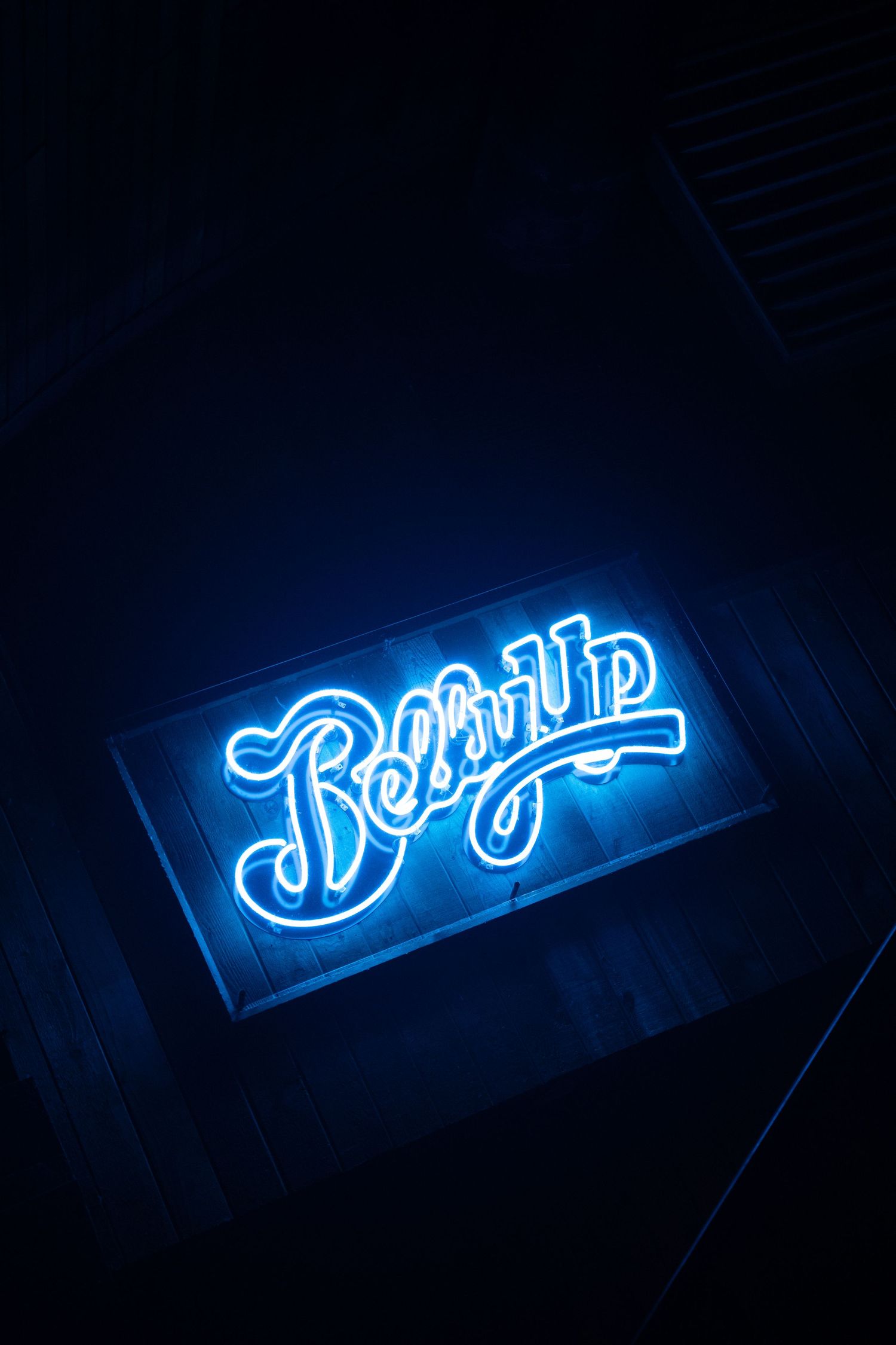 Neon blue cursive text sign glowing in the dark displaying artistic lettering at different angles.