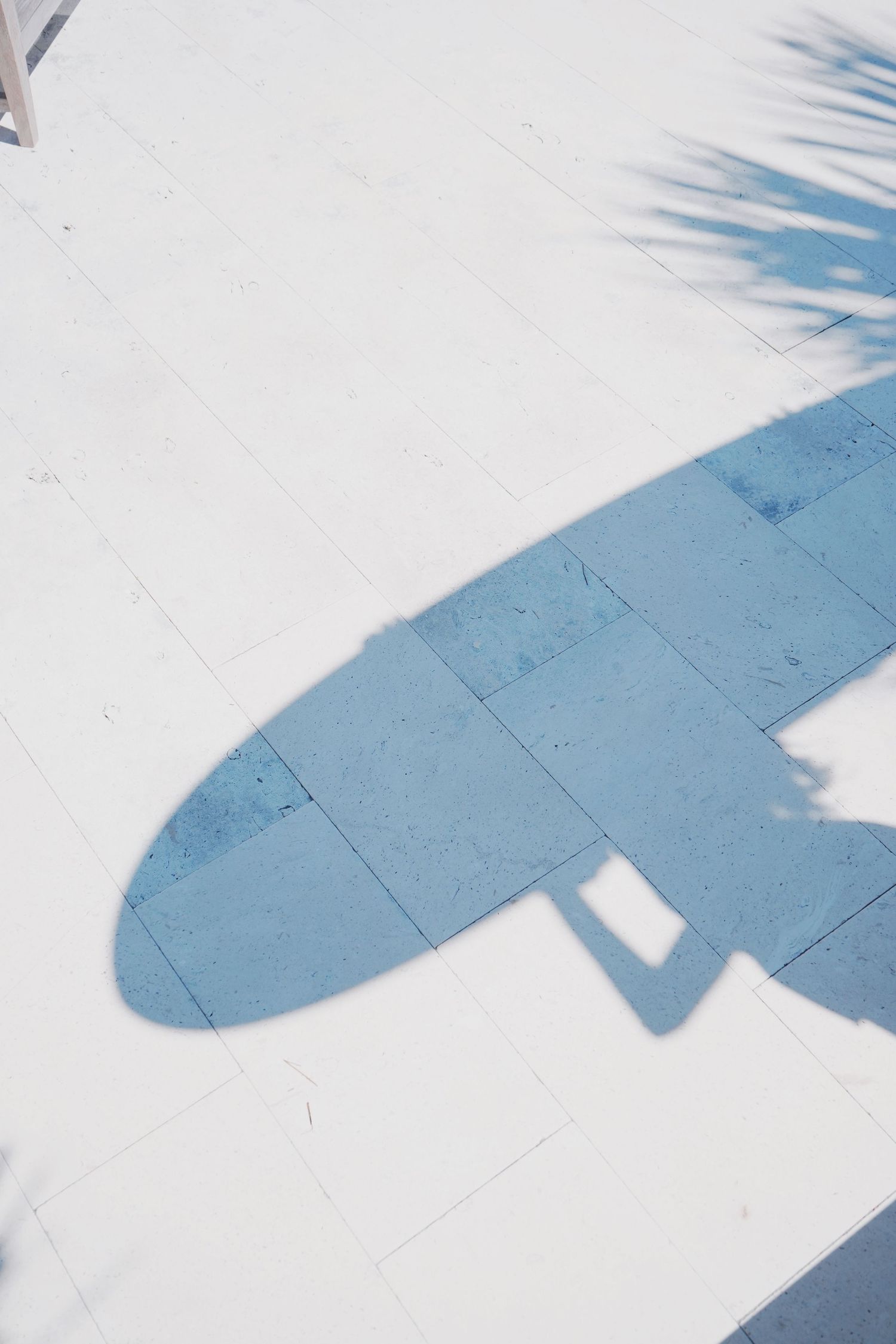 Shadow silhouette of a surfboard cast on white pavement on a sunny day.