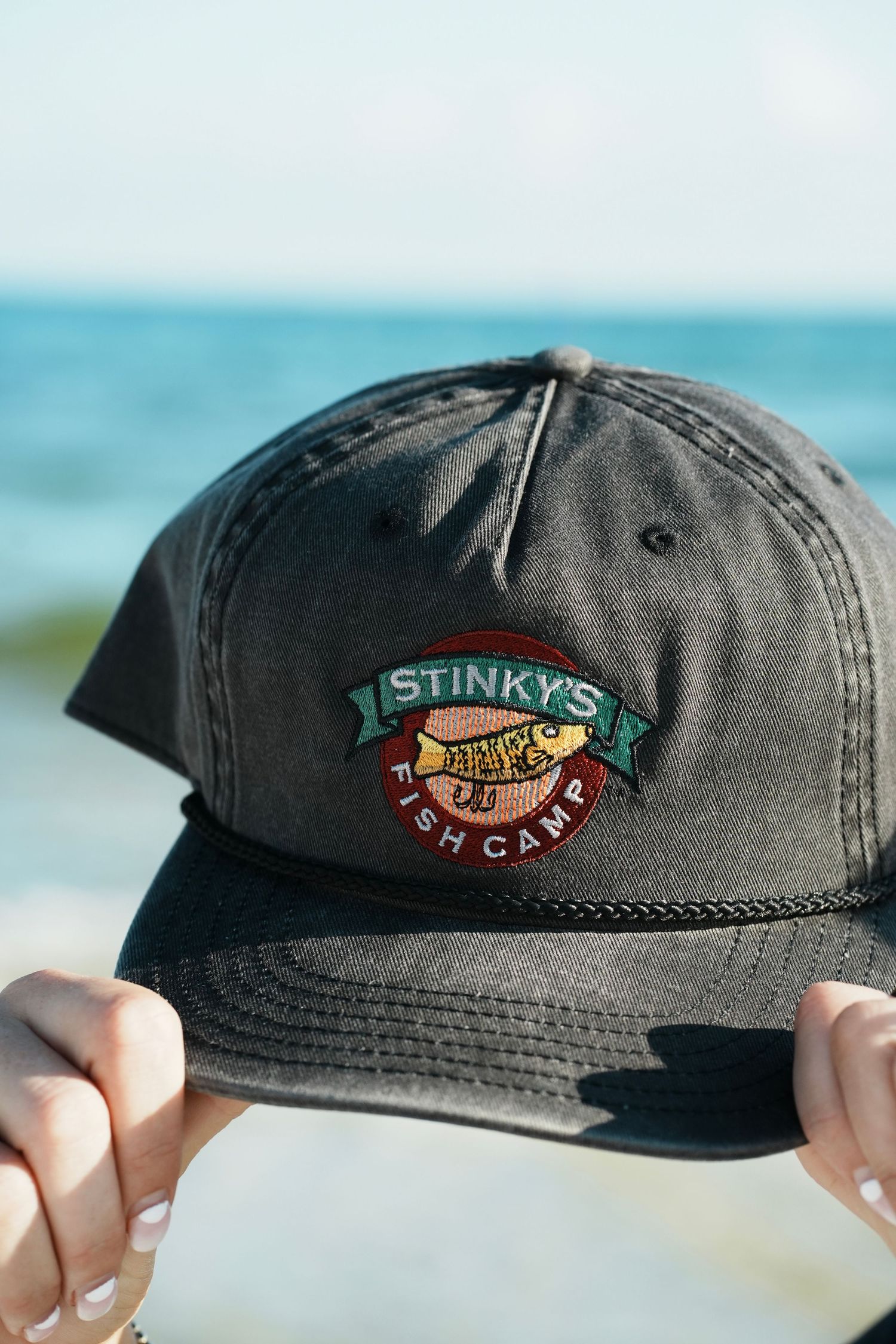 A video sequence showing multiple angles of a dark gray baseball cap with an embroidered Stinky's Fish Camp logo patch.