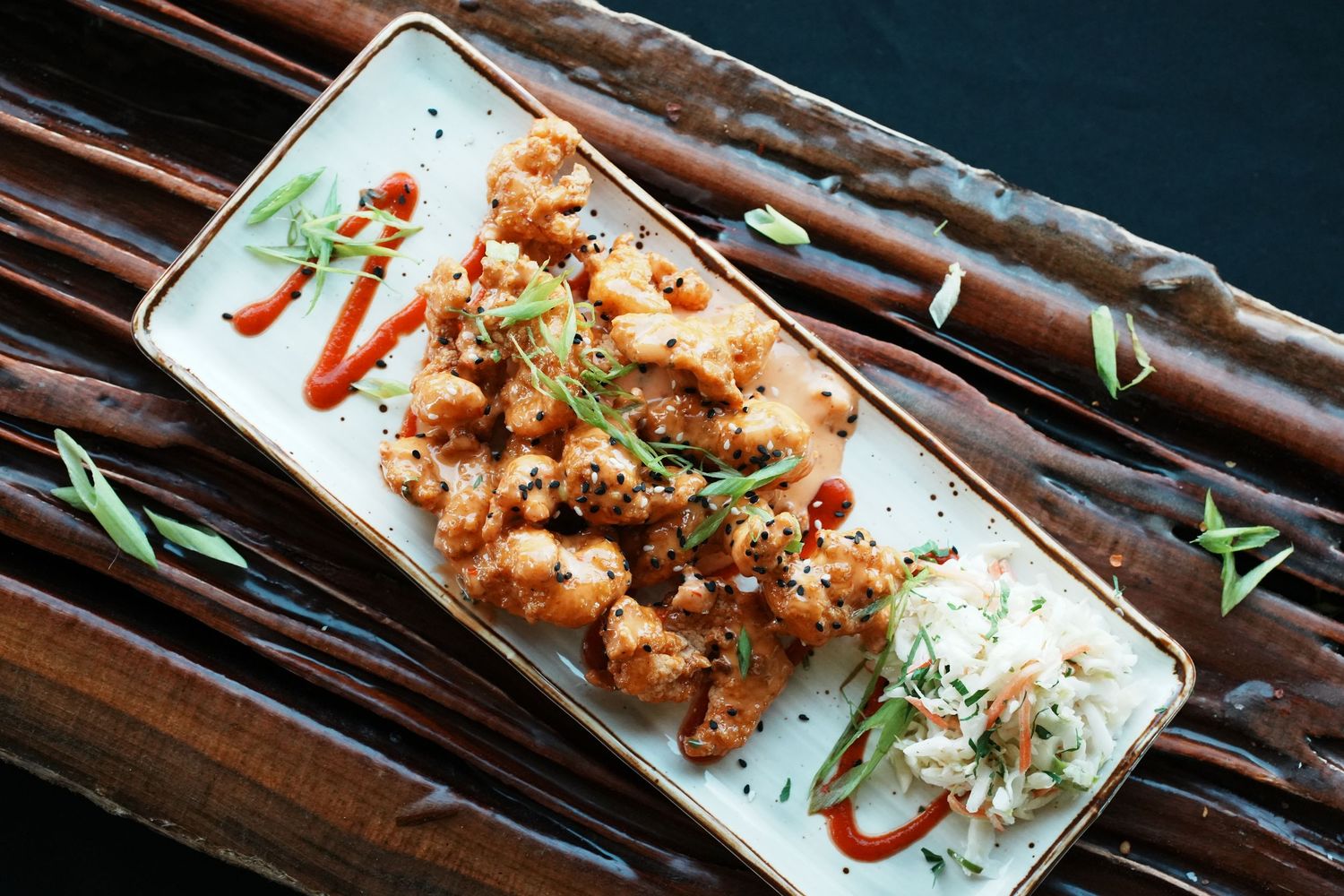 Six rectangular white plates with various Asian appetizers and sauces arranged on dark bamboo placemats.