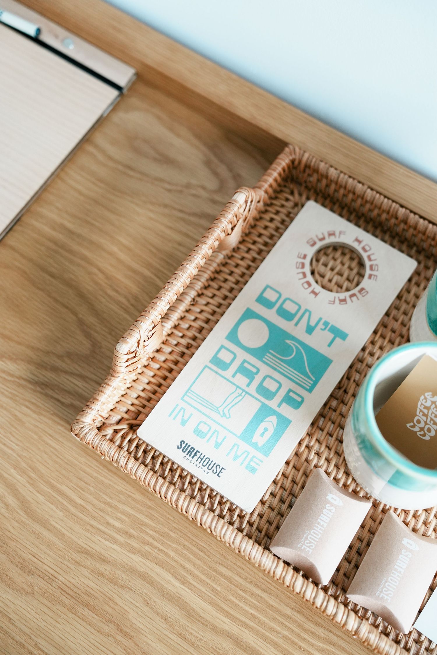 Woven rattan tray with turquoise and white books arranged in a minimalist style on wooden surface.