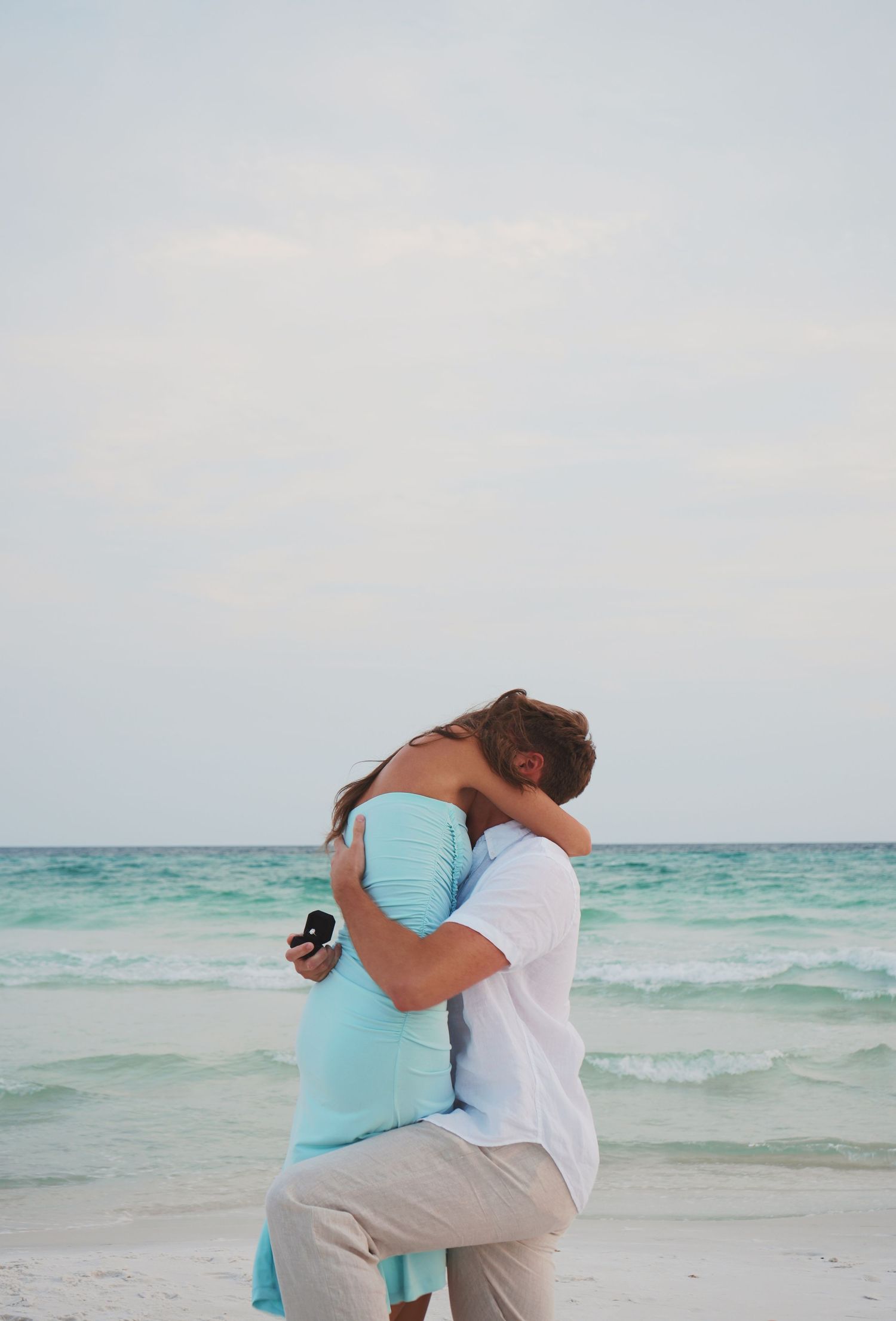 Couple sharing a romantic moment on a beautiful beach with turquoise waters and white sand in the background.