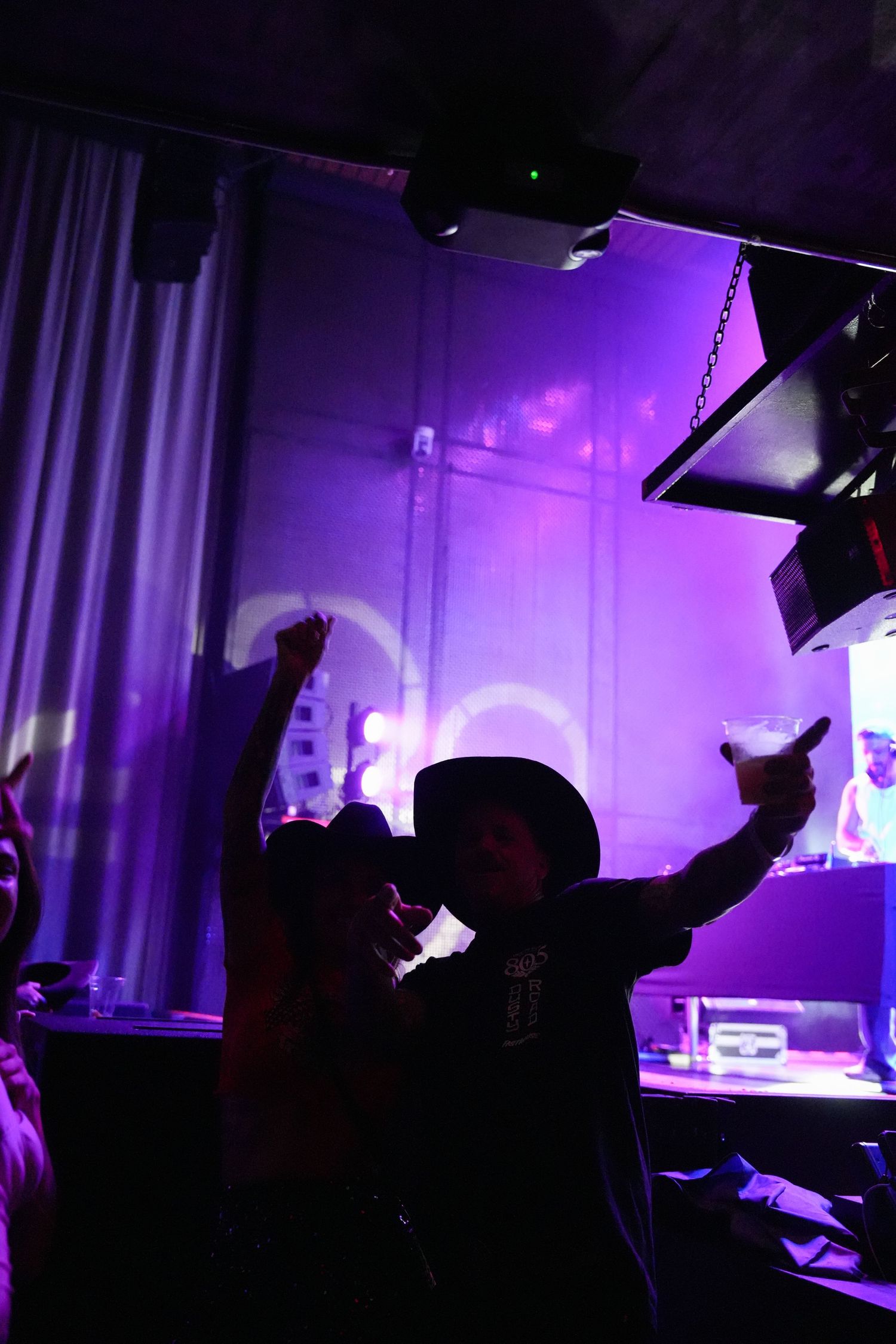 Silhouettes of people dancing and partying in a nightclub with purple lighting and atmospheric effects.