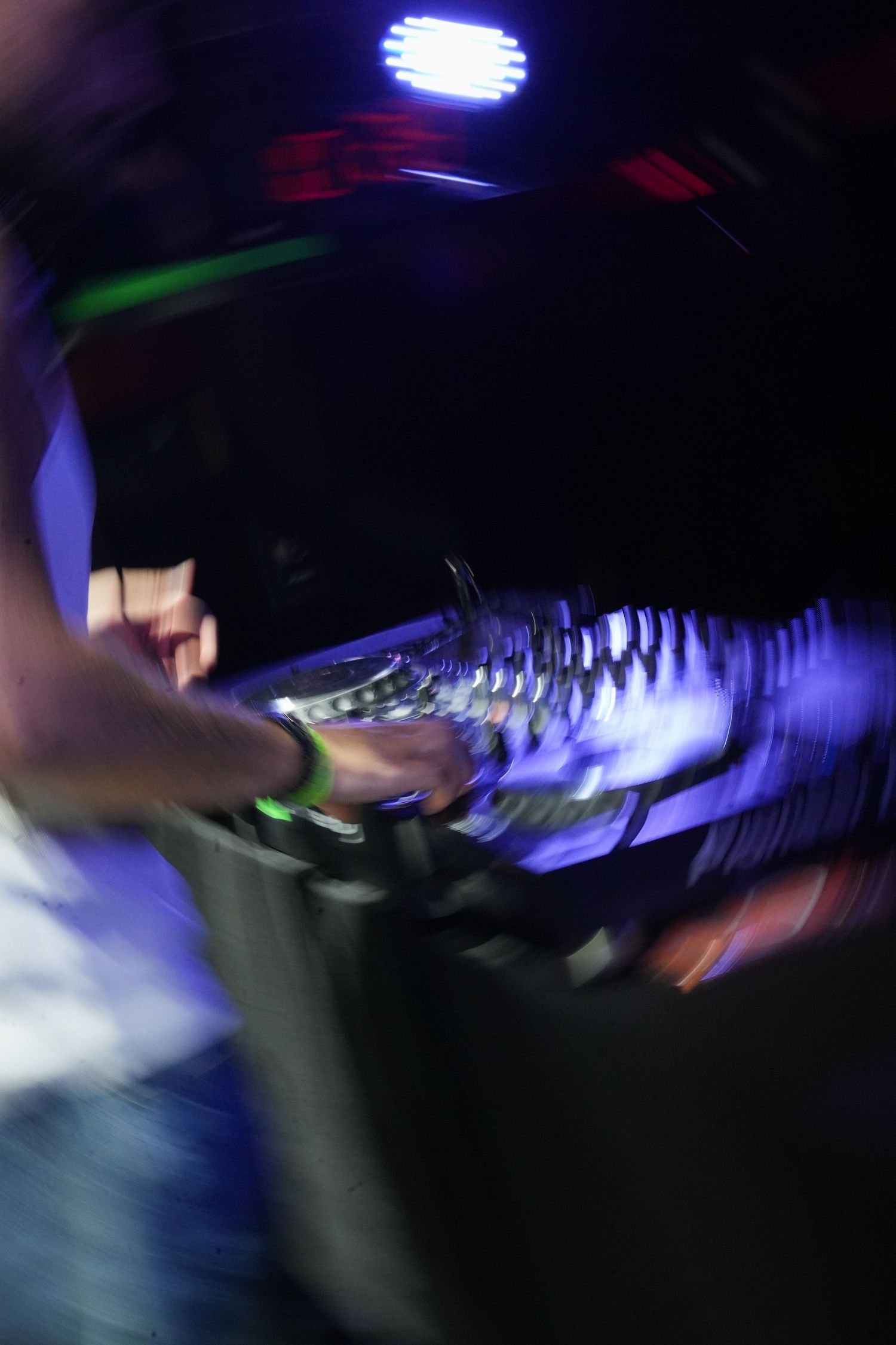 Blurred motion shot of a DJ performing at a nightclub with blue lighting and mixing equipment.