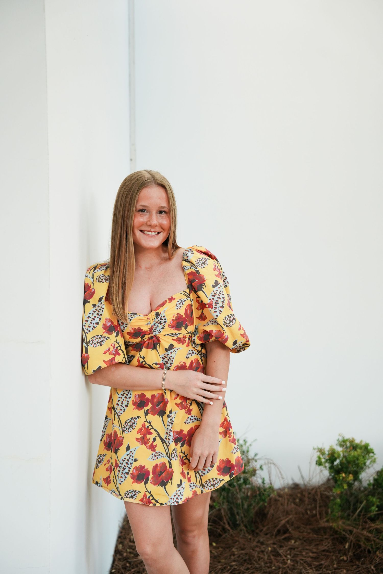 A series of photos showing someone in a bright floral patterned yellow dress against a white wall with landscaping.