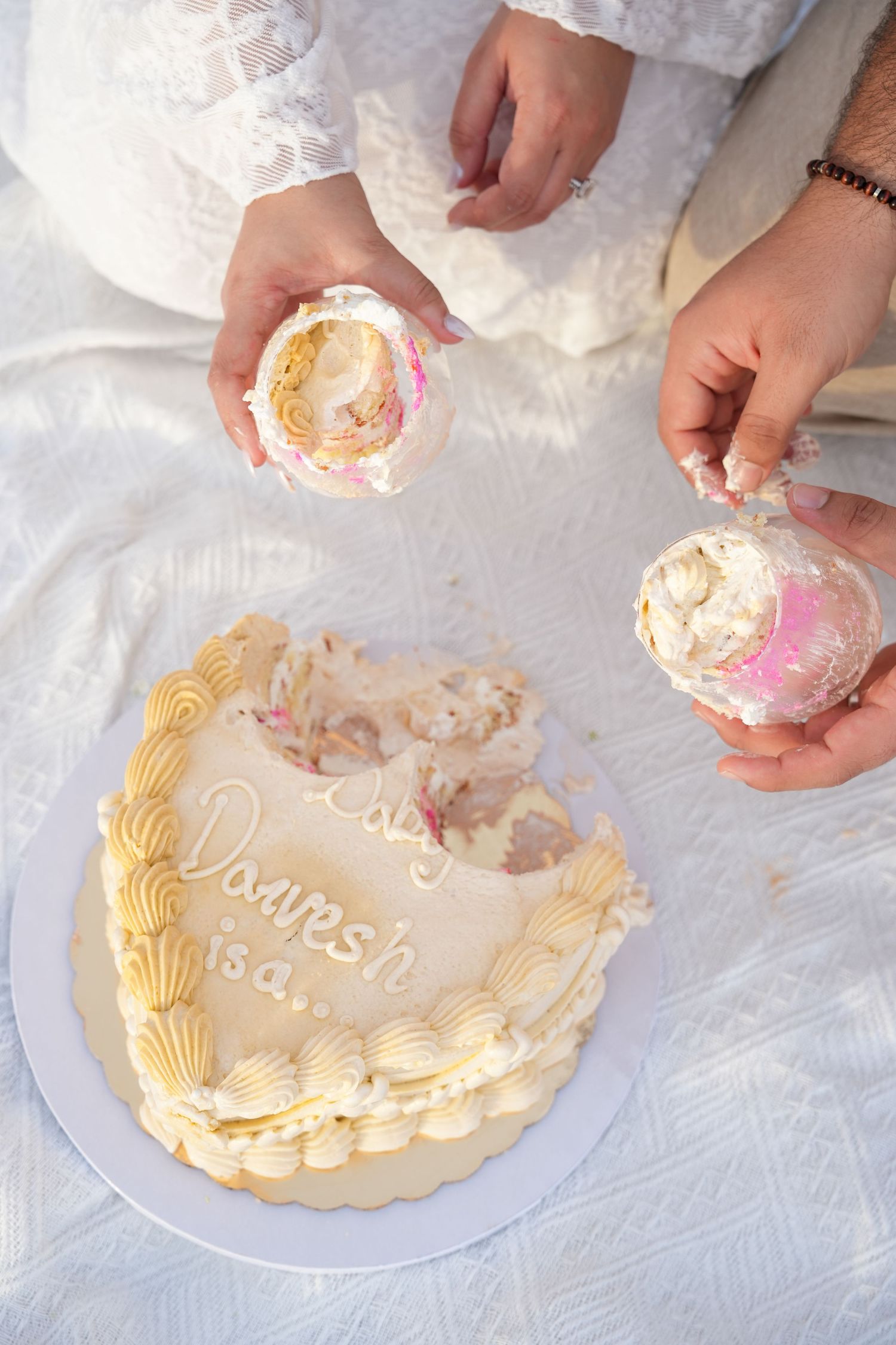 Couple cutting a heart-shaped wedding cake decorated with shells and cream, inscribed with names Dayesh and Lisa.