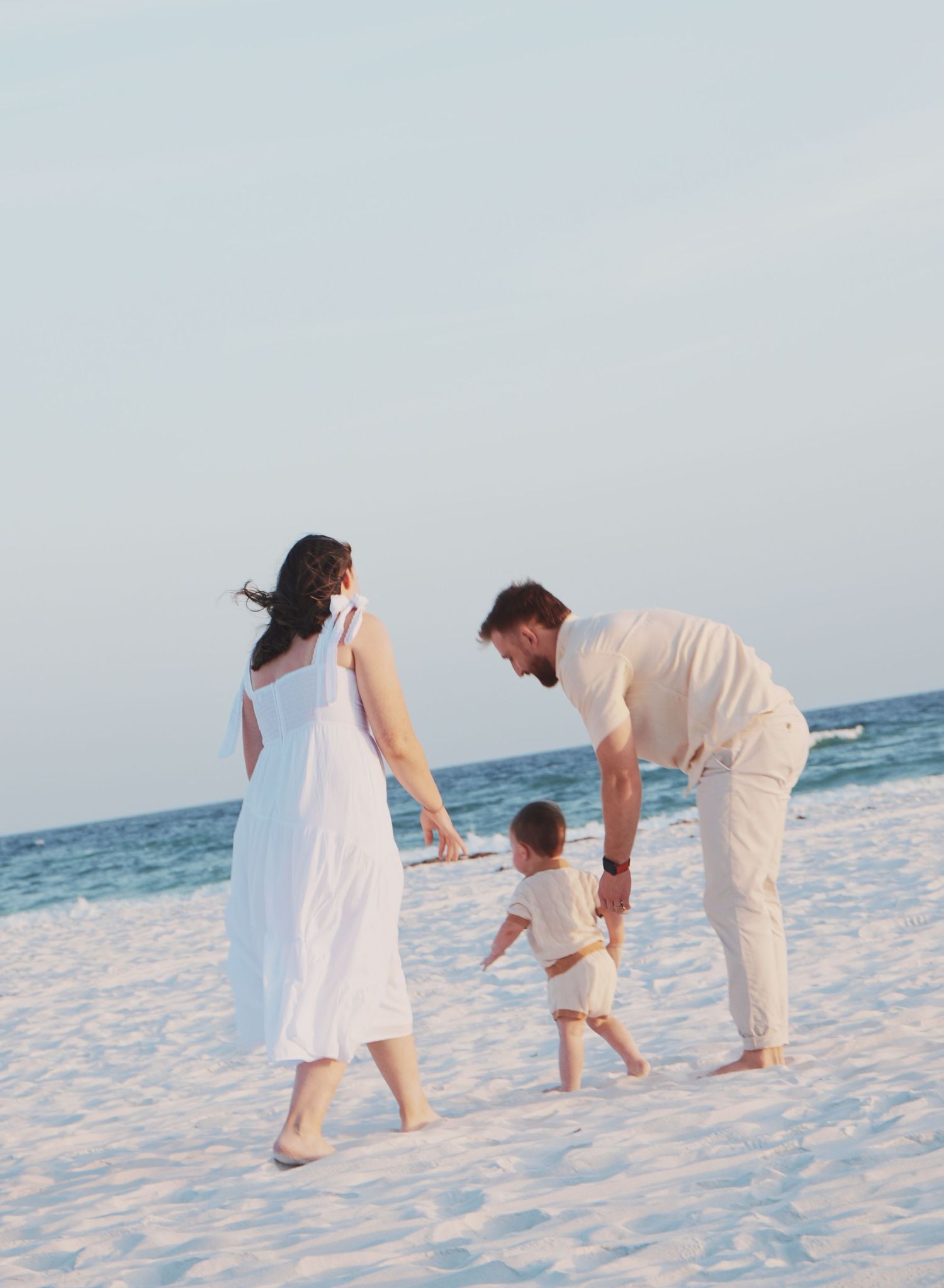 Family dressed in white plays together on pristine white sand beach at sunset.