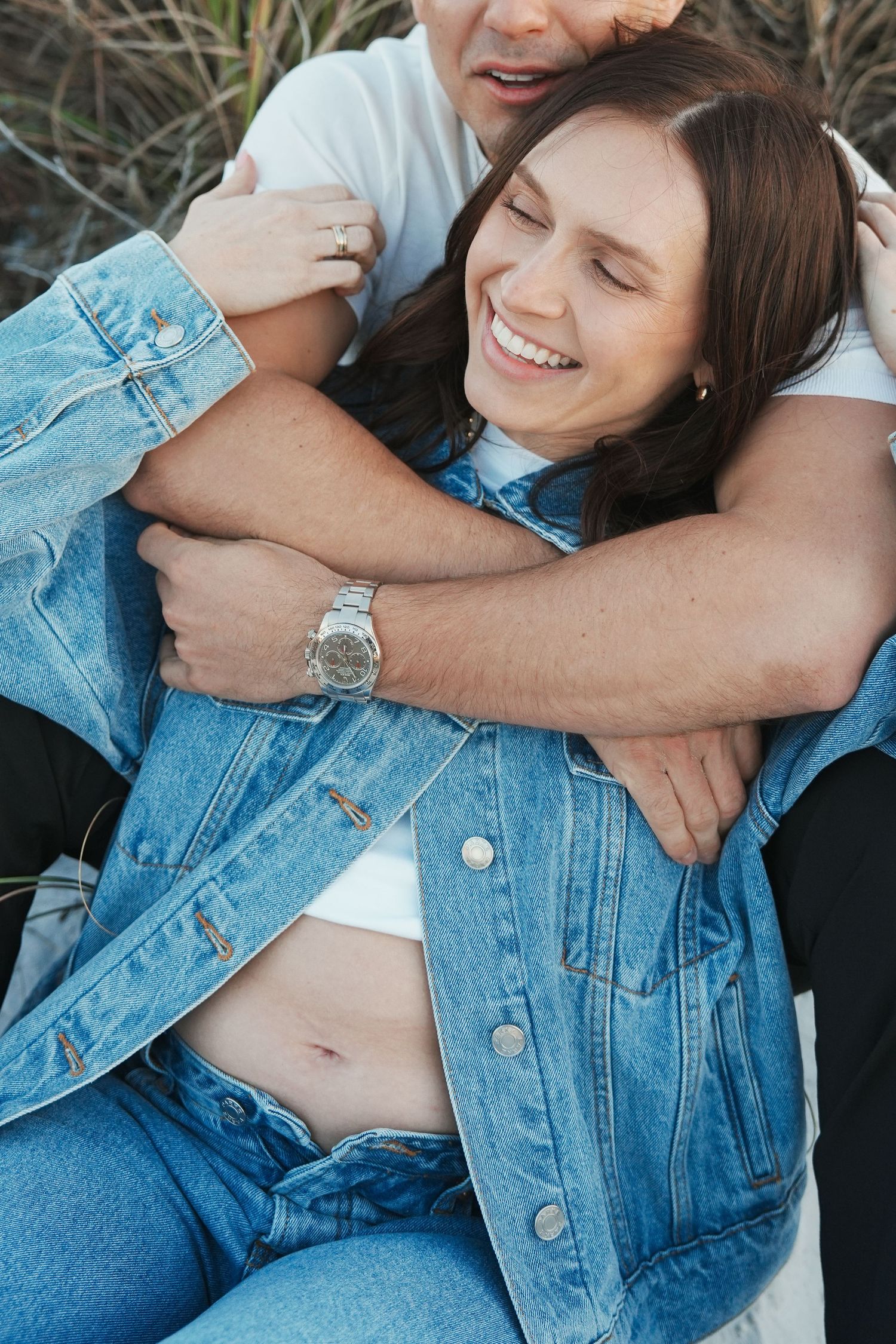 A couple embraces and laughs while wearing matching denim outfits in an intimate outdoor portrait.