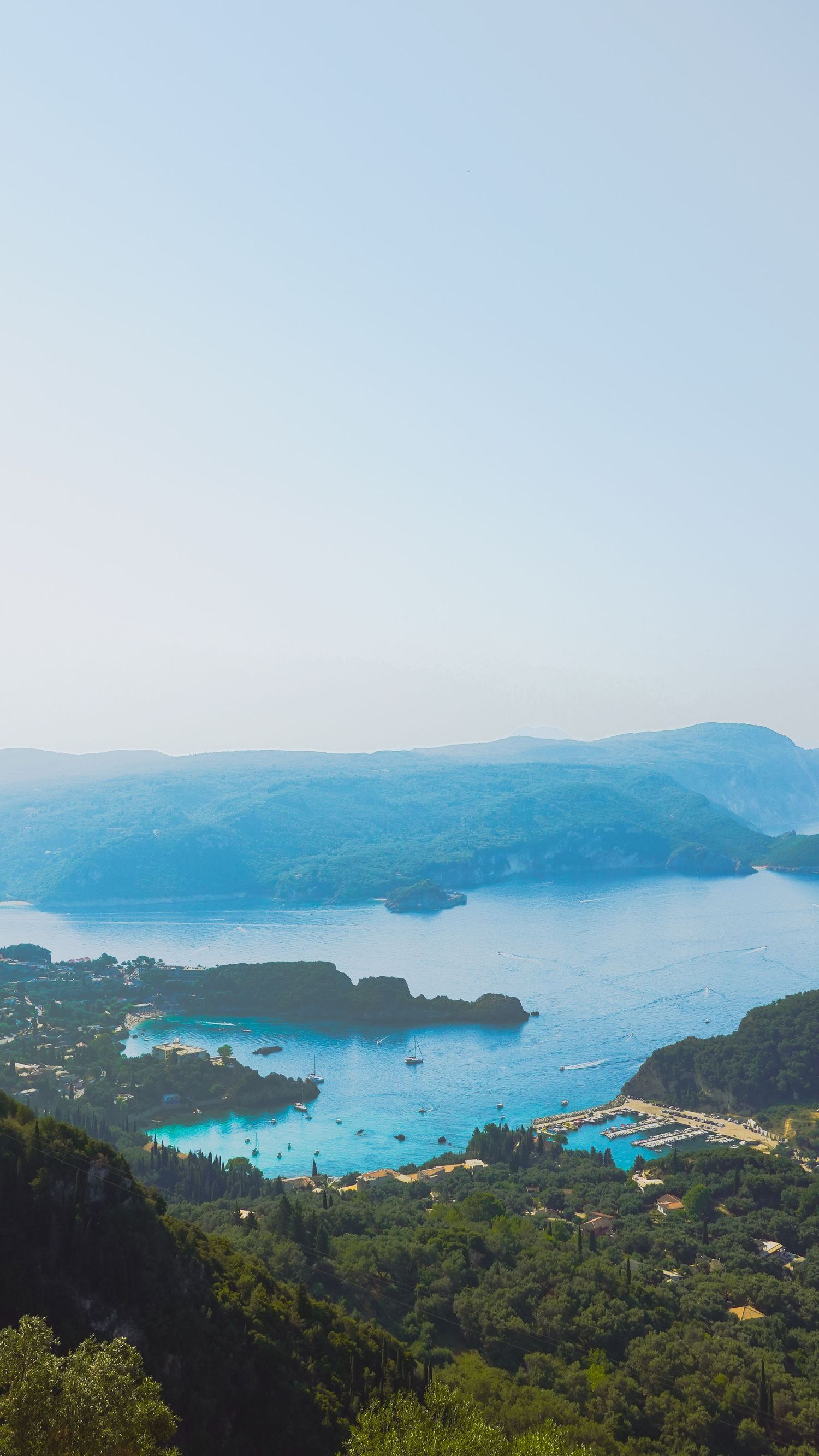 Aerial view of a coastal Mediterranean bay with turquoise waters surrounded by lush green hills.
