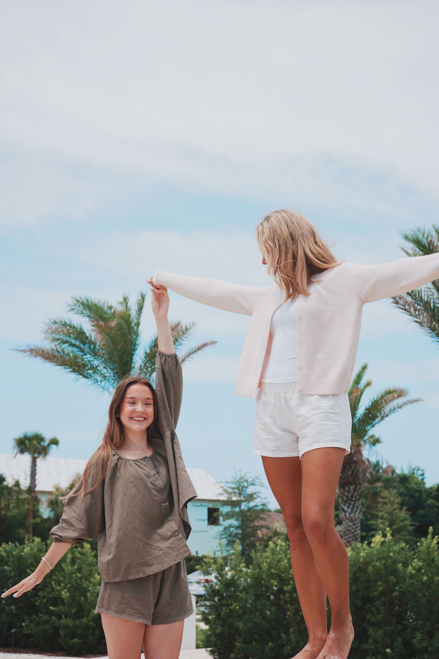 Two friends enjoying a carefree moment outdoors with palm trees and blue sky in the background.