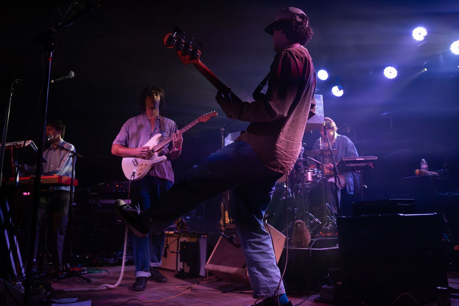 Musicians perform on a dark stage with blue lighting during a live concert performance.
