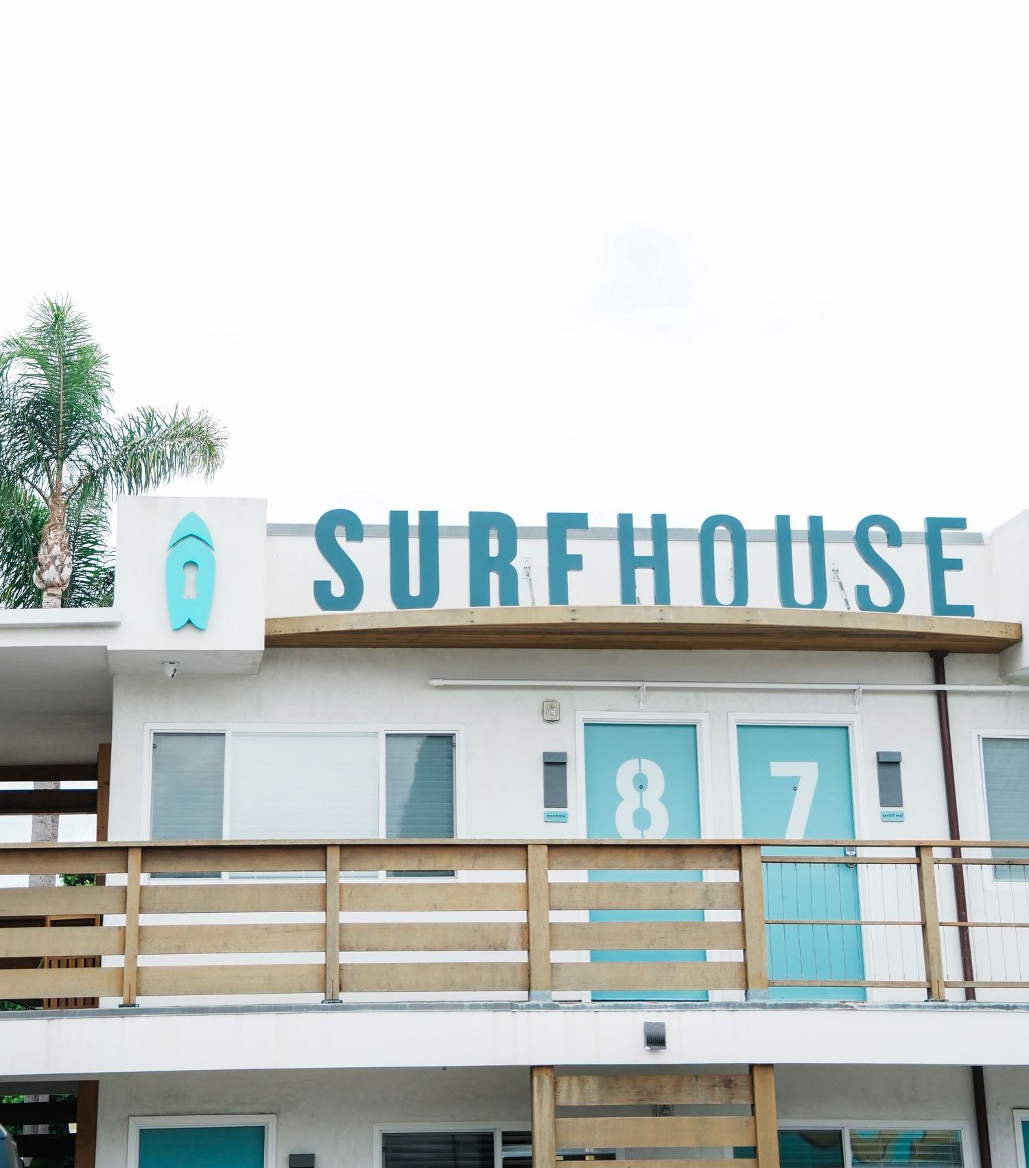 A retro-style surfhouse motel exterior with turquoise blue signage and horizontal wooden slats along the facade.