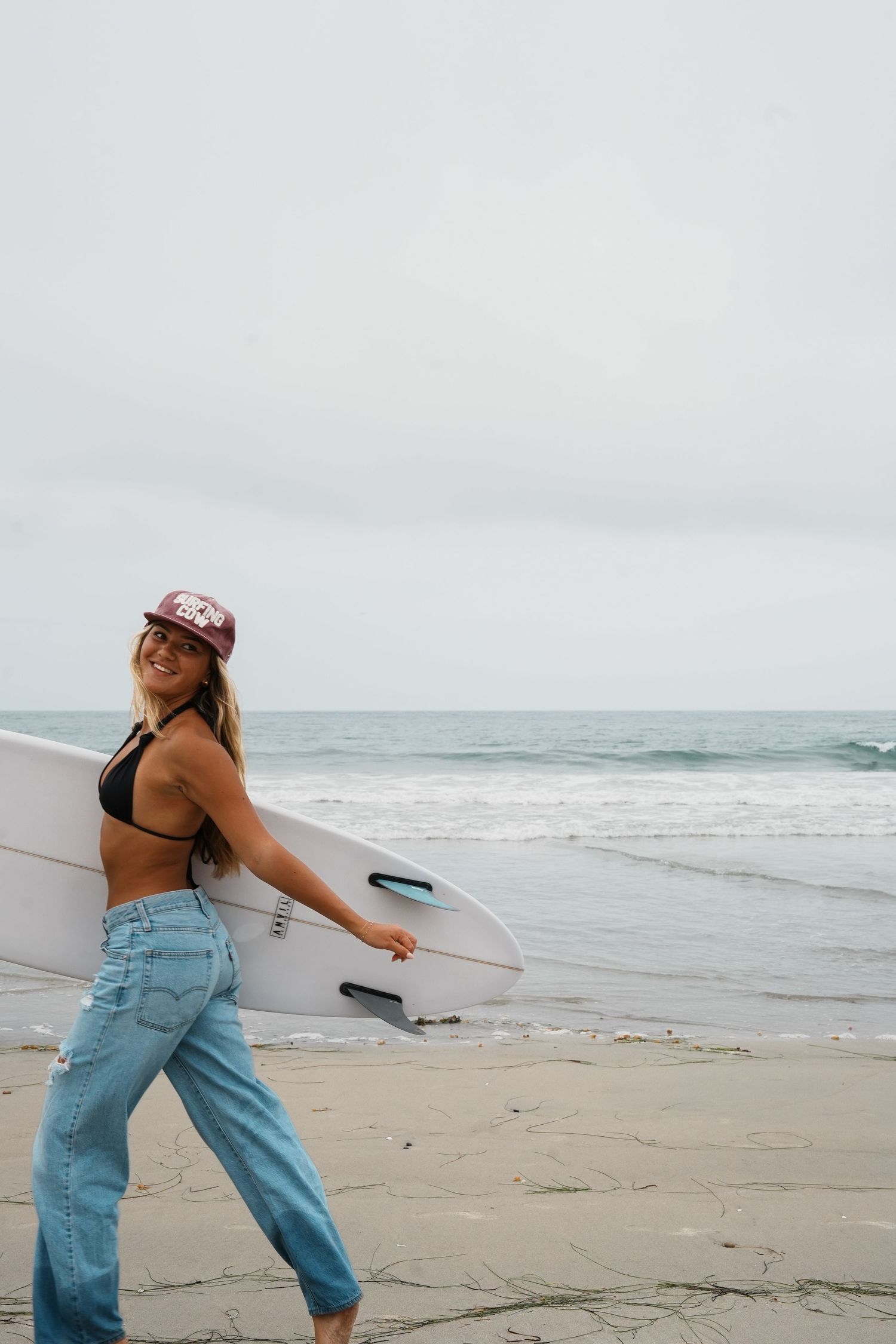 Surfer carrying white surfboard on beach during overcast day.
