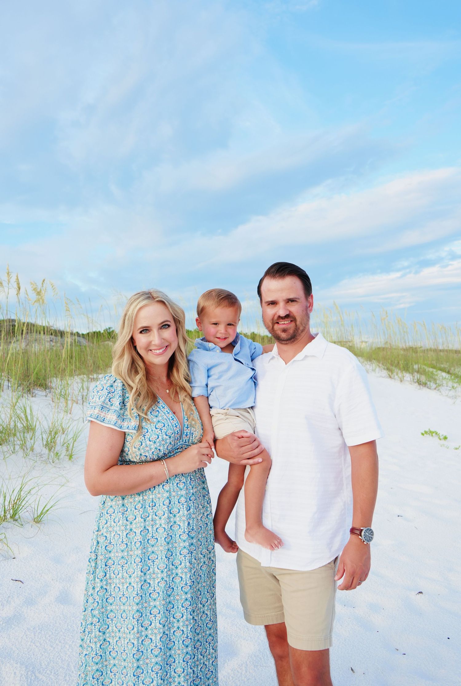 Family enjoying a sunny day at the white sand beach with sea grass and bright blue sky.