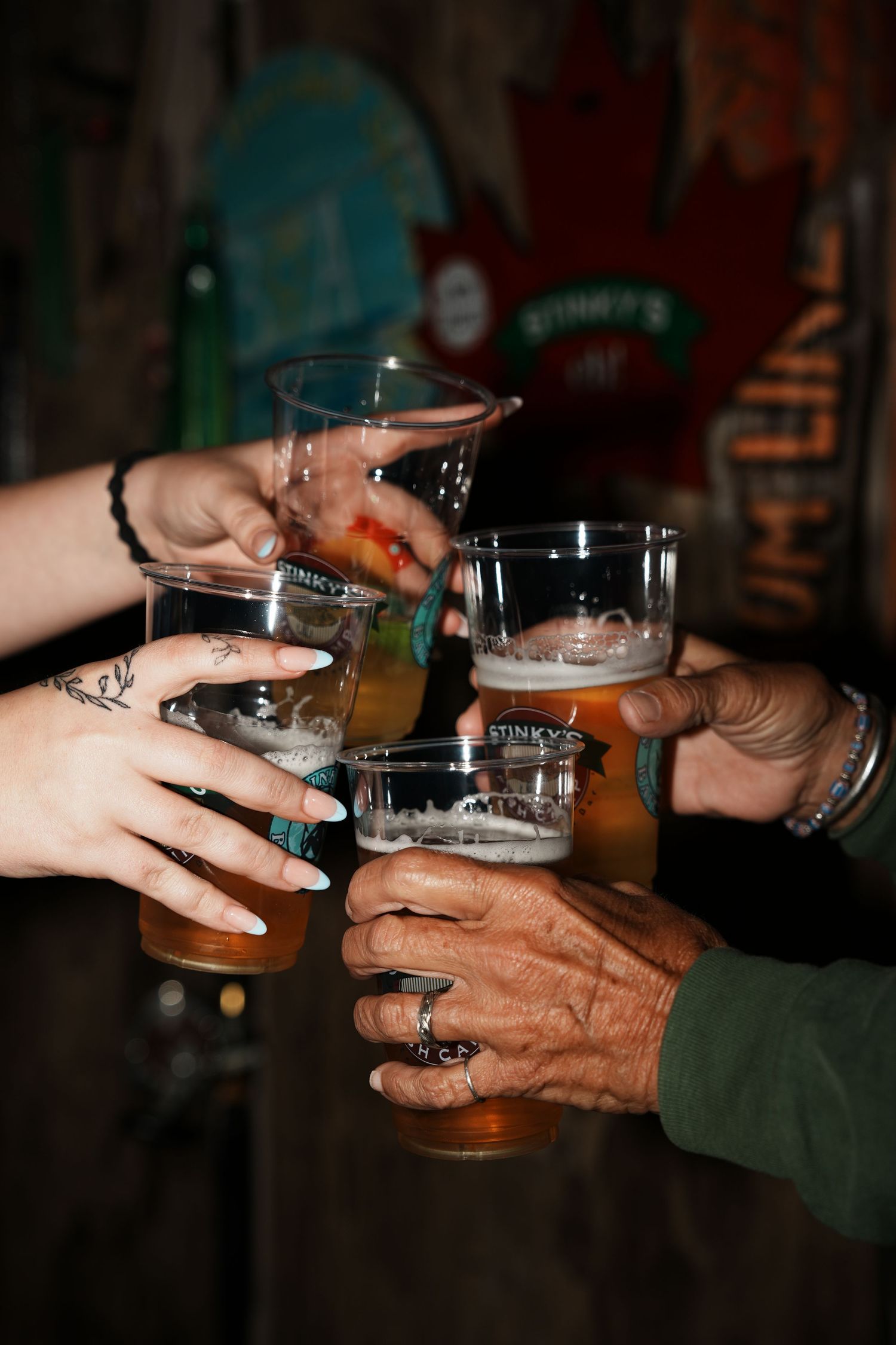 Hands holding and toasting with various beer glasses in a dimly lit setting.
