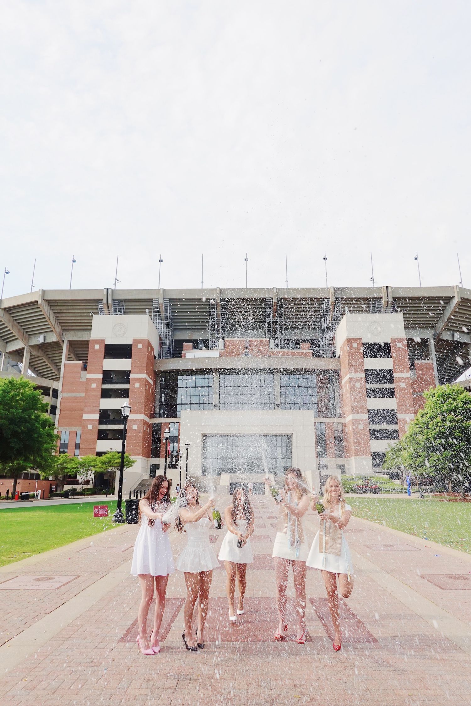 A group celebrates with pink confetti outside a brick stadium entrance in a sequence of four connected photos.