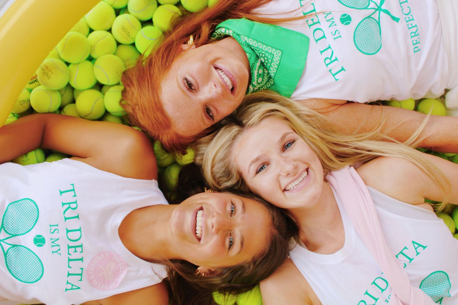 Three people lying down surrounded by green tennis balls in matching team shirts.
