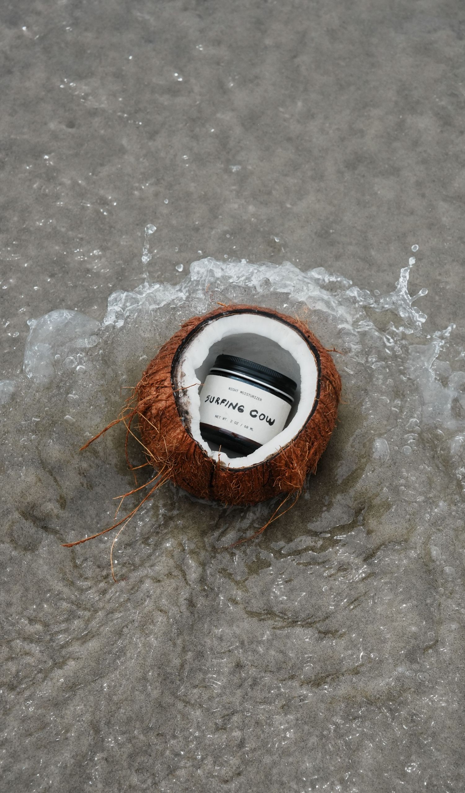 Product container placed inside split coconut on wet concrete surface.