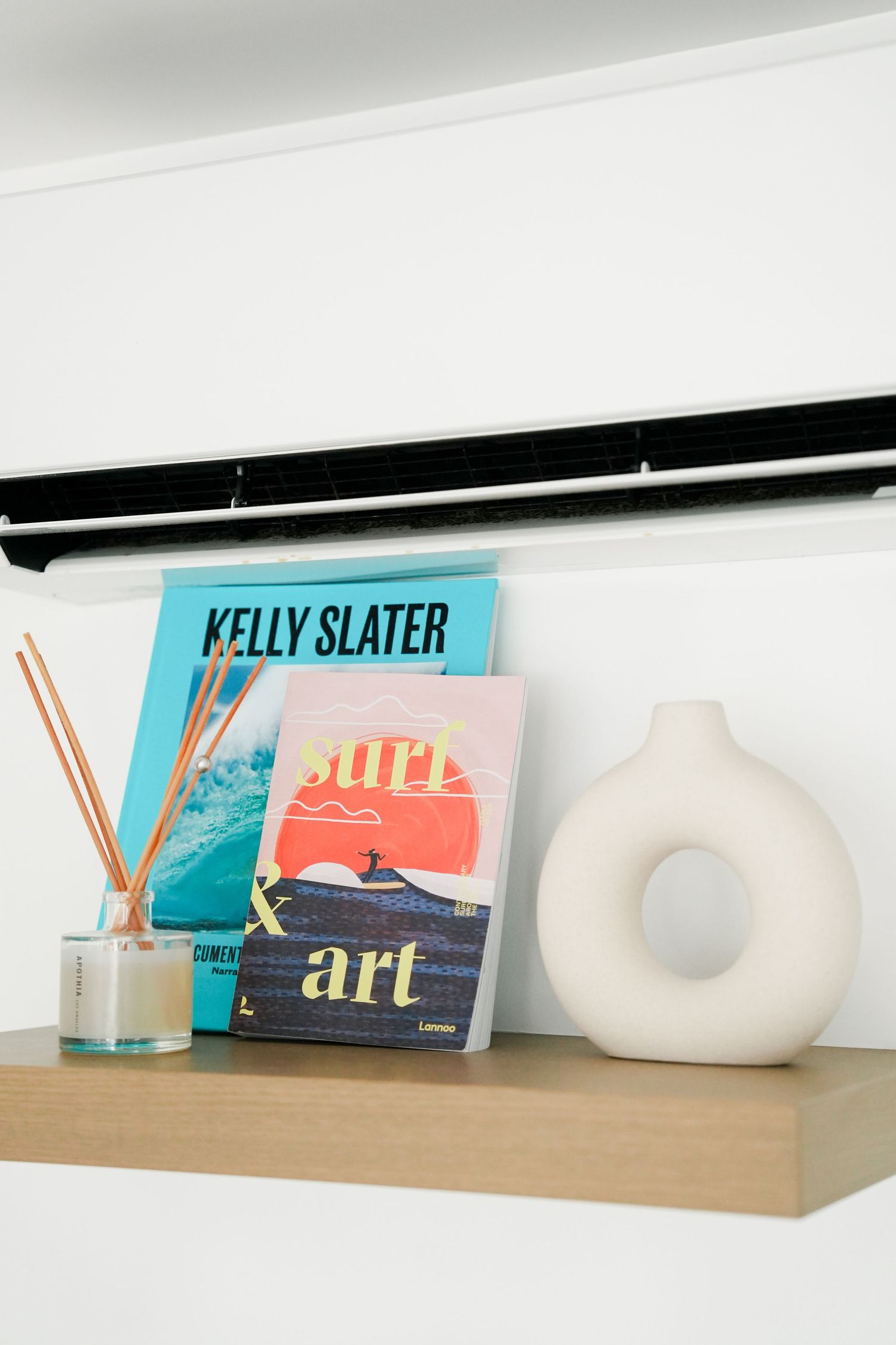Modern white shelf displays colorful art books and decorative ceramic objects against a minimalist wall.