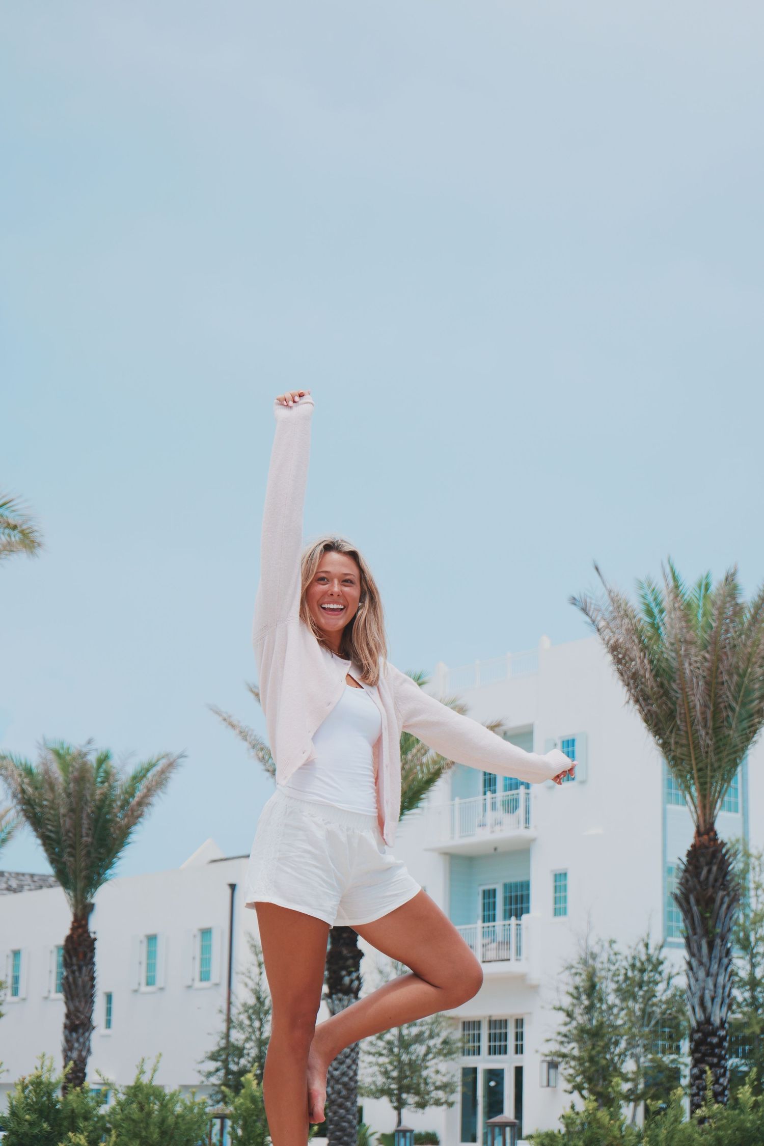 A series of photos set against an architectural backdrop with palm trees shows someone in white summer attire creating playful poses.