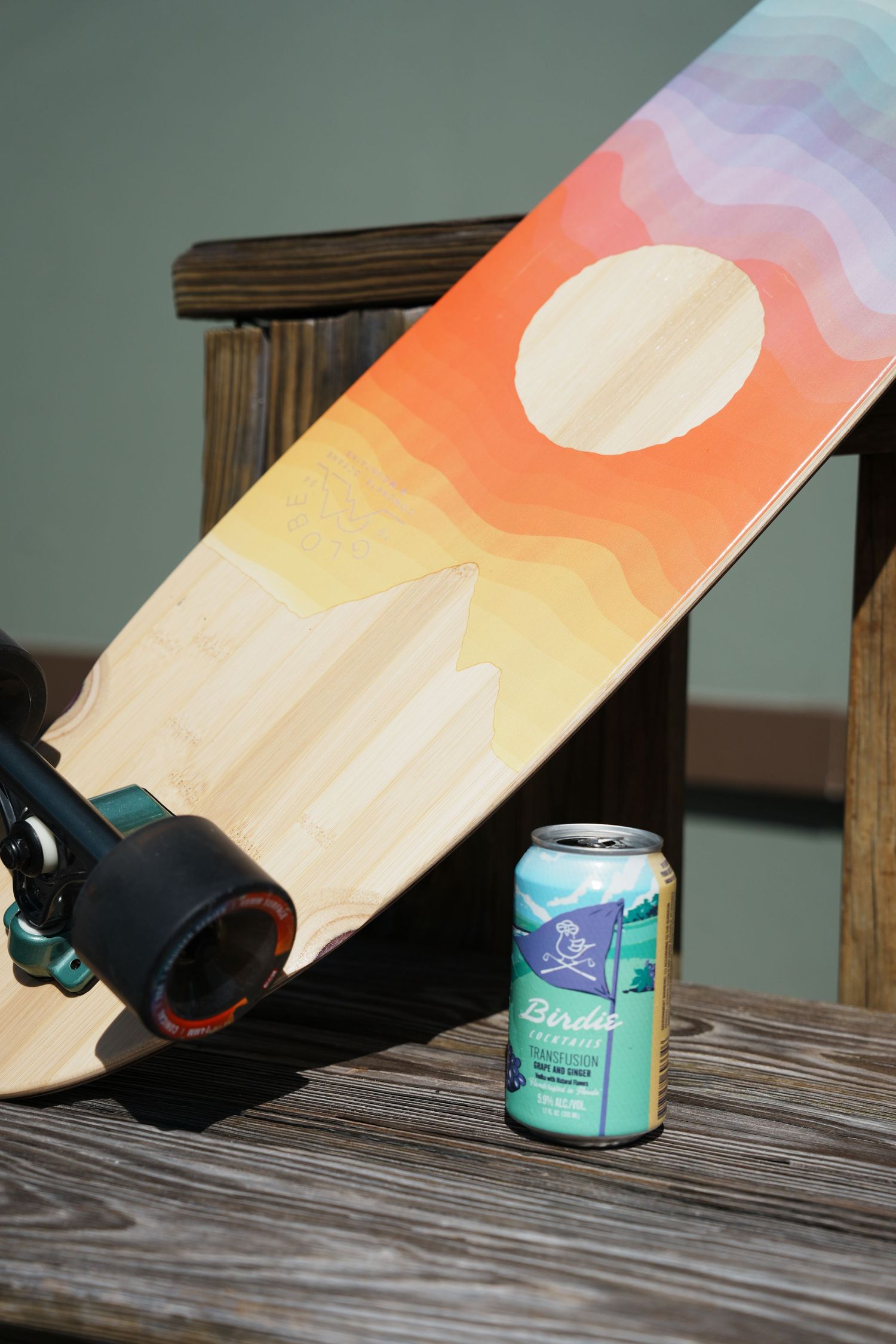 Colorful painted skateboard deck propped against cans of beverage on a weathered wooden surface.