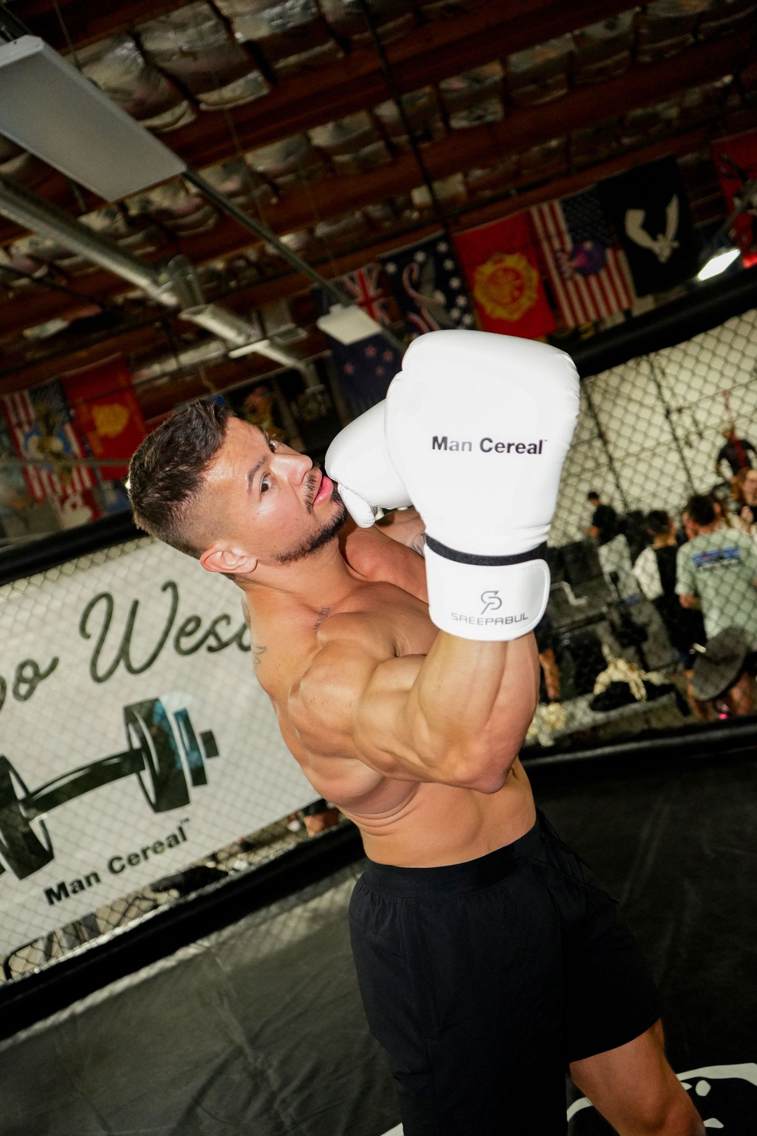 Muscular athlete in black tank top drinks from a white container during workout at gym.