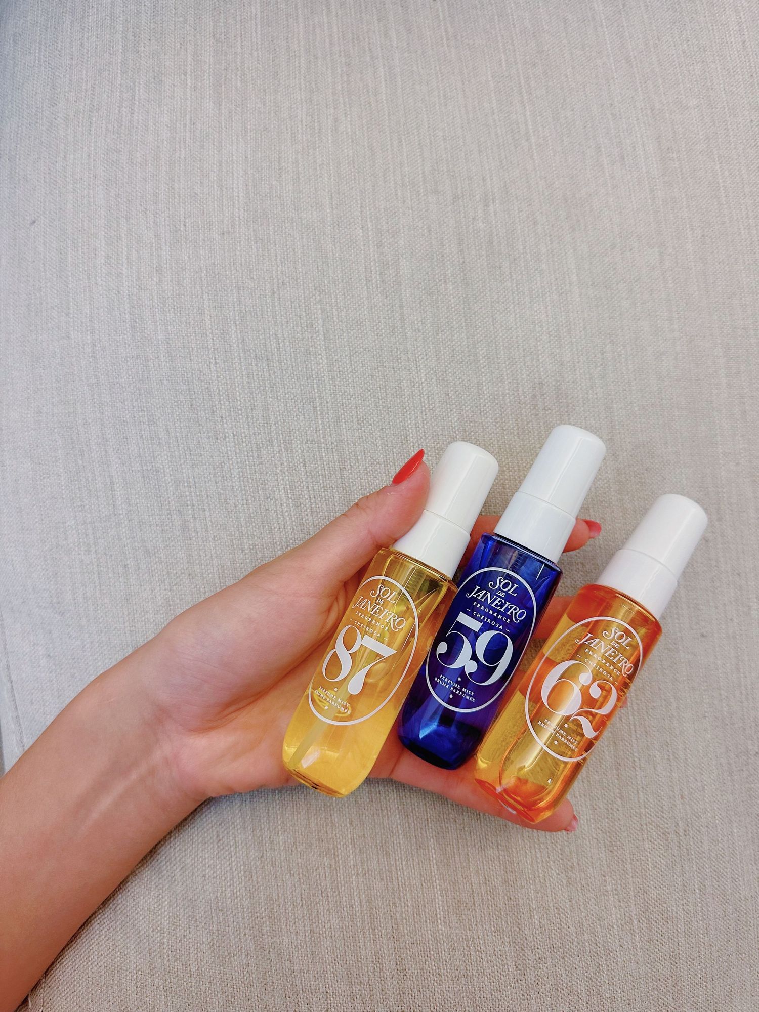 Three colorful beauty product bottles in yellow, blue, and orange held against grey background.