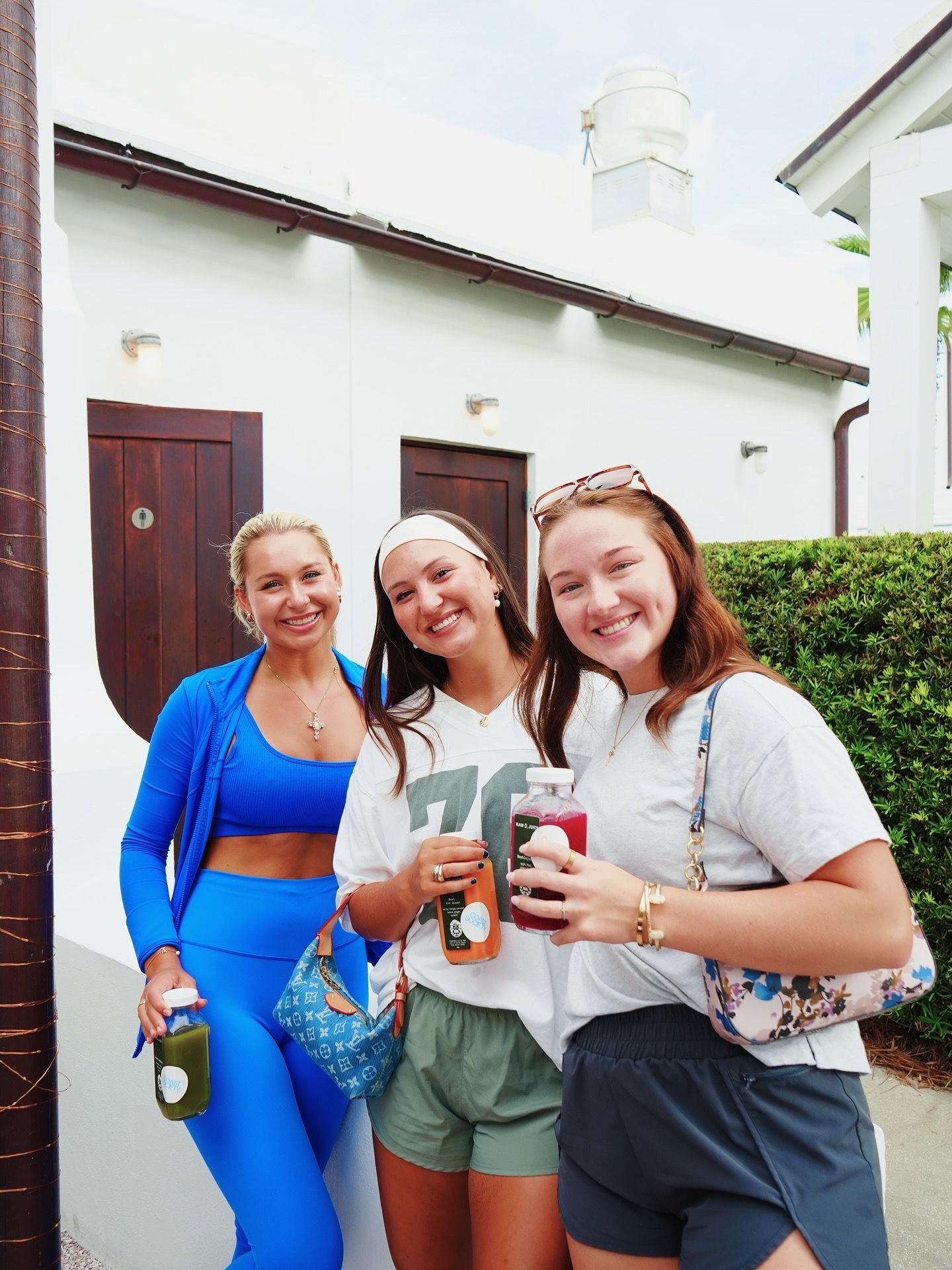 Three friends enjoying drinks while gathered outside of a white building with brown doors.