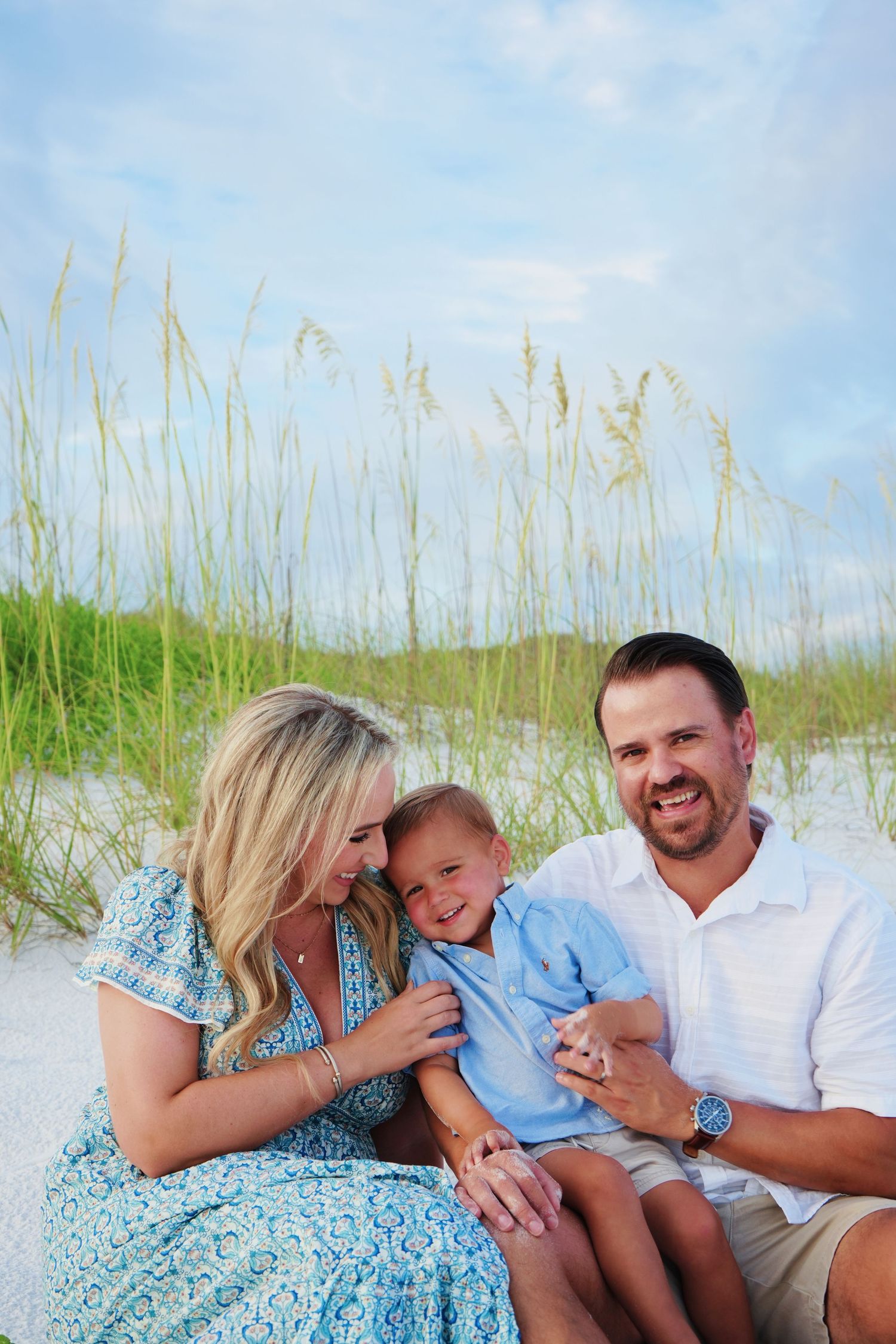 Family enjoys playful moments together while sitting in beach grass near the ocean.