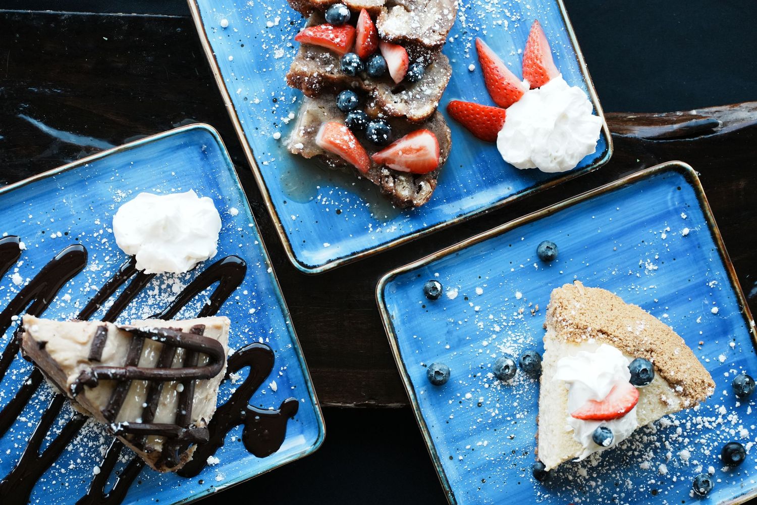 Overhead view of three blue plates with desserts including cake and whipped cream.