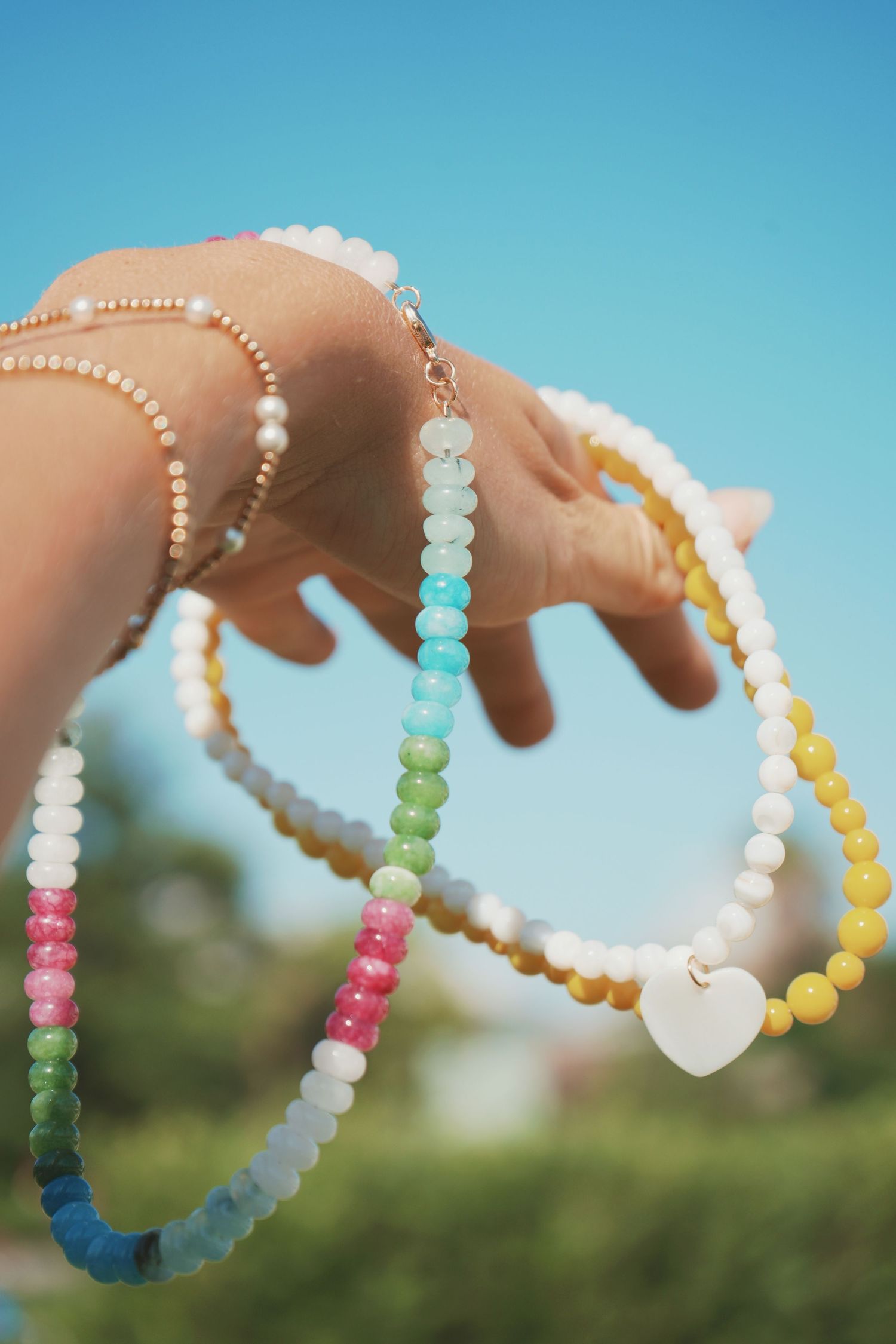 Colorful beaded bracelets displayed against a bright blue sky and green foliage background.