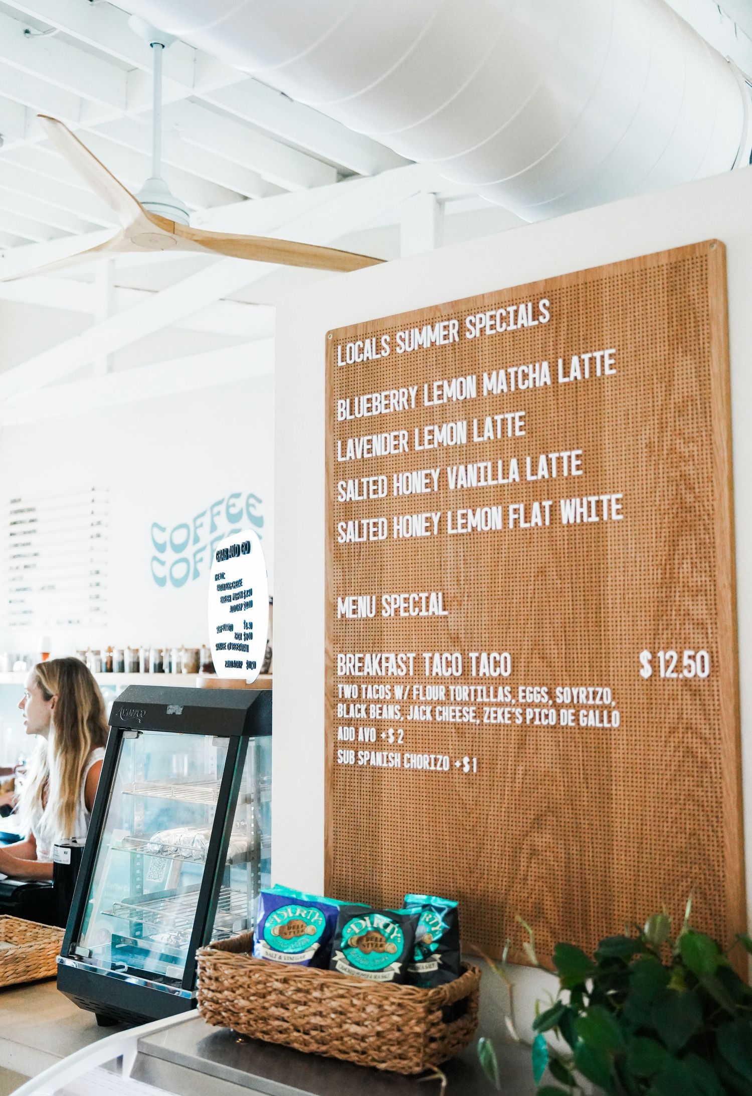 Wooden menu board displays specialty coffee drinks and prices in a bright cafe interior.