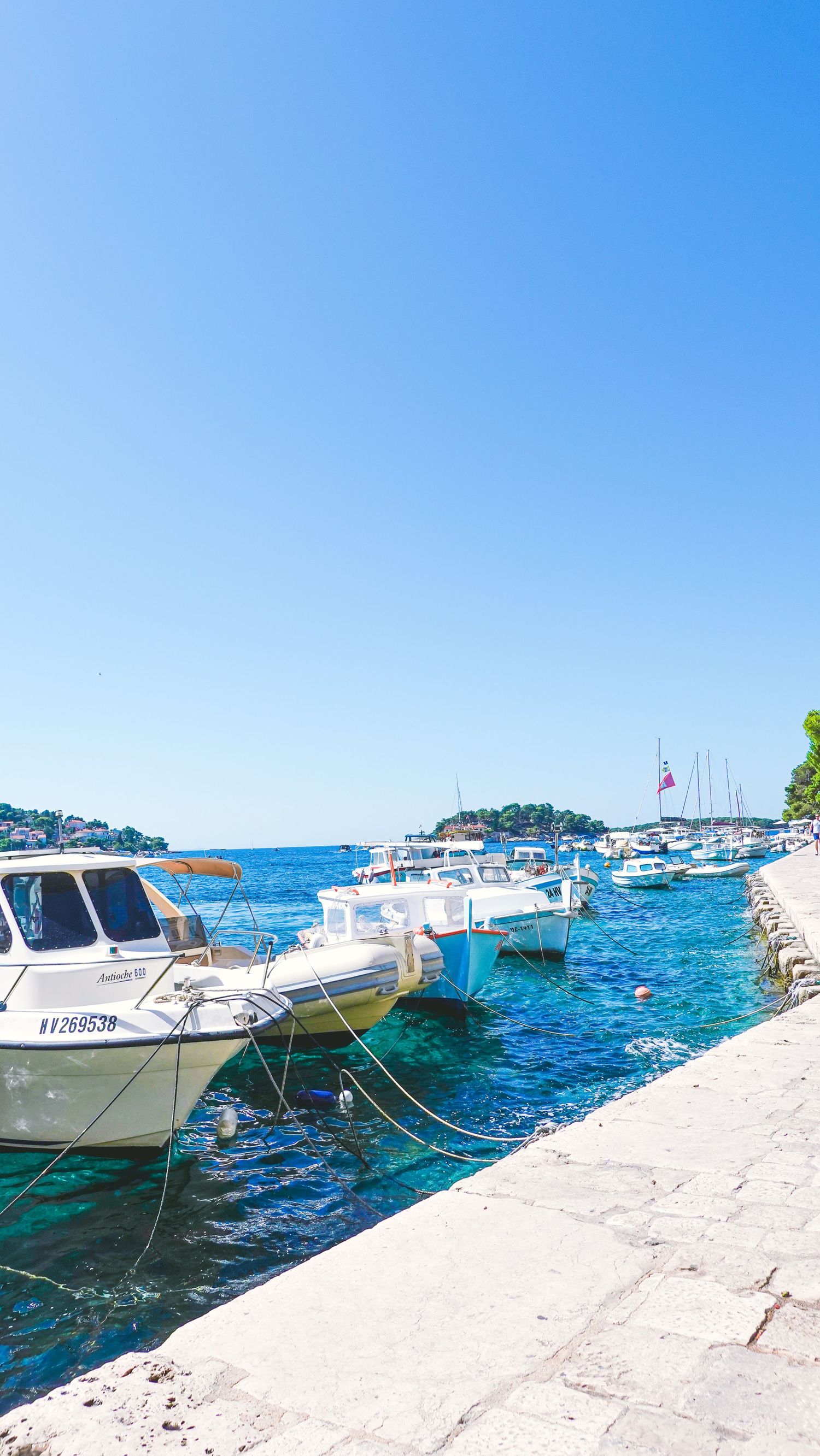 White boats moored along stone pier in crystal clear Mediterranean waters. European prints