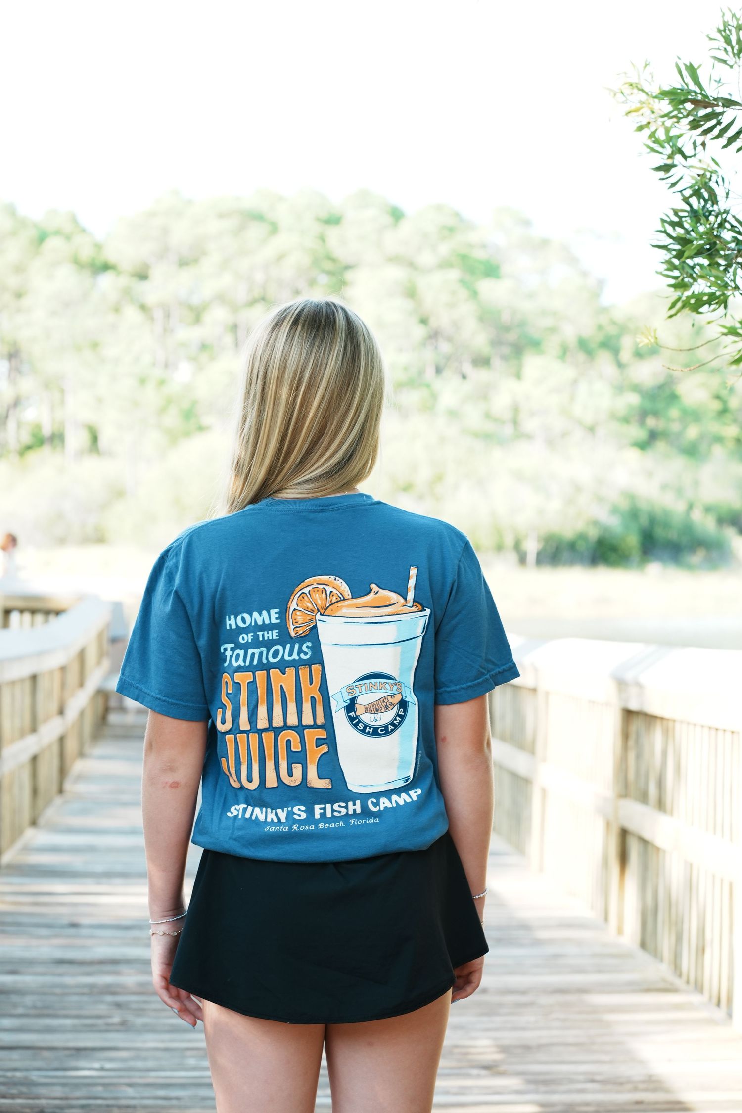 Back view of person wearing blue t-shirt with fish camp design walking on wooden boardwalk.