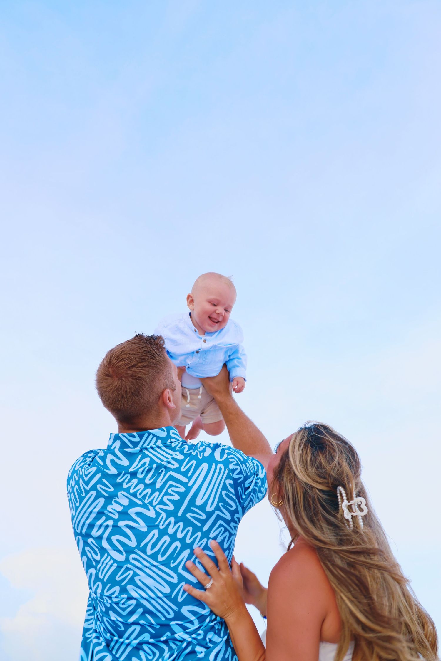 Family shares joyful moment against blue sky background at the beach.