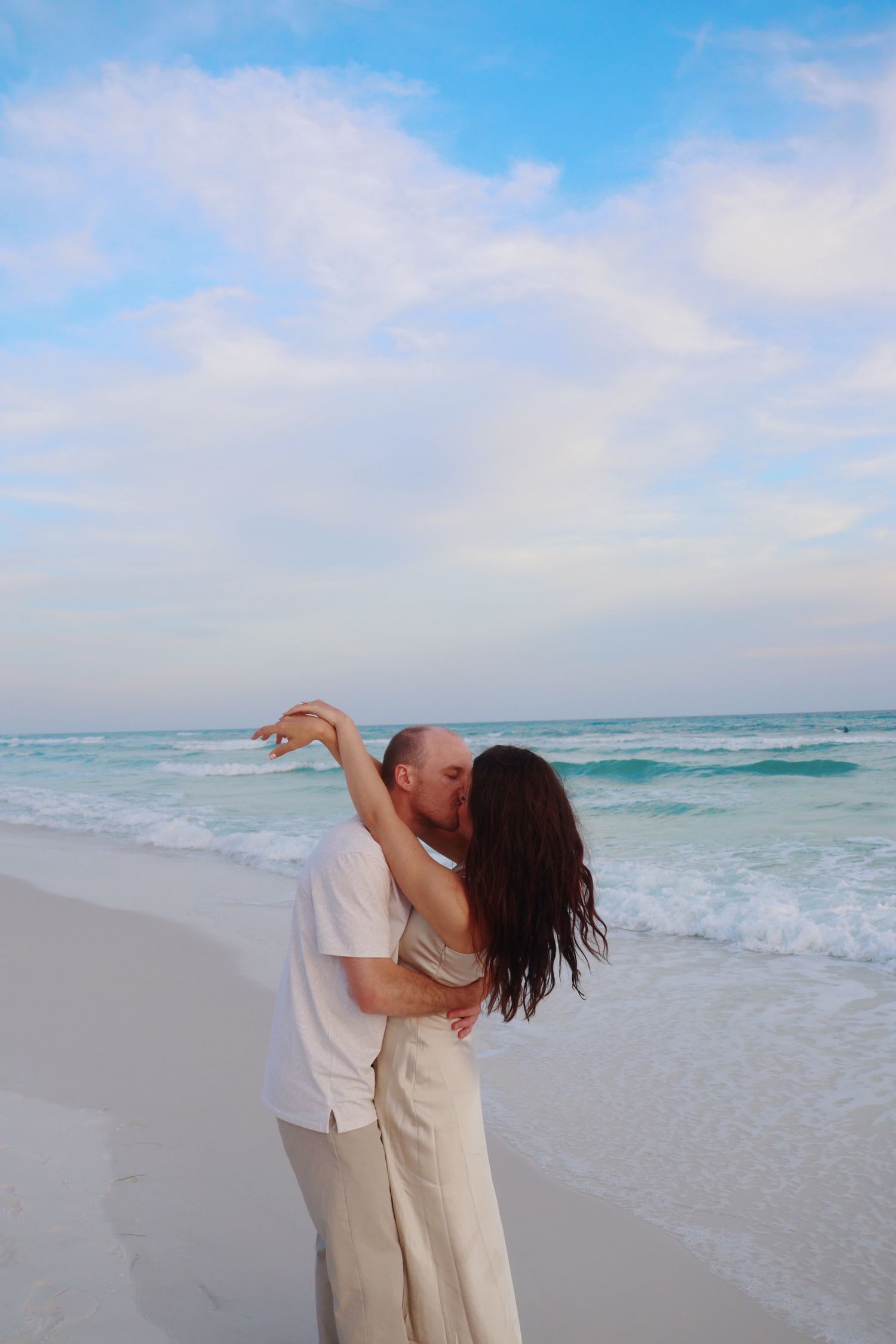 Romantic dance pose on a beach with turquoise waves in the background.